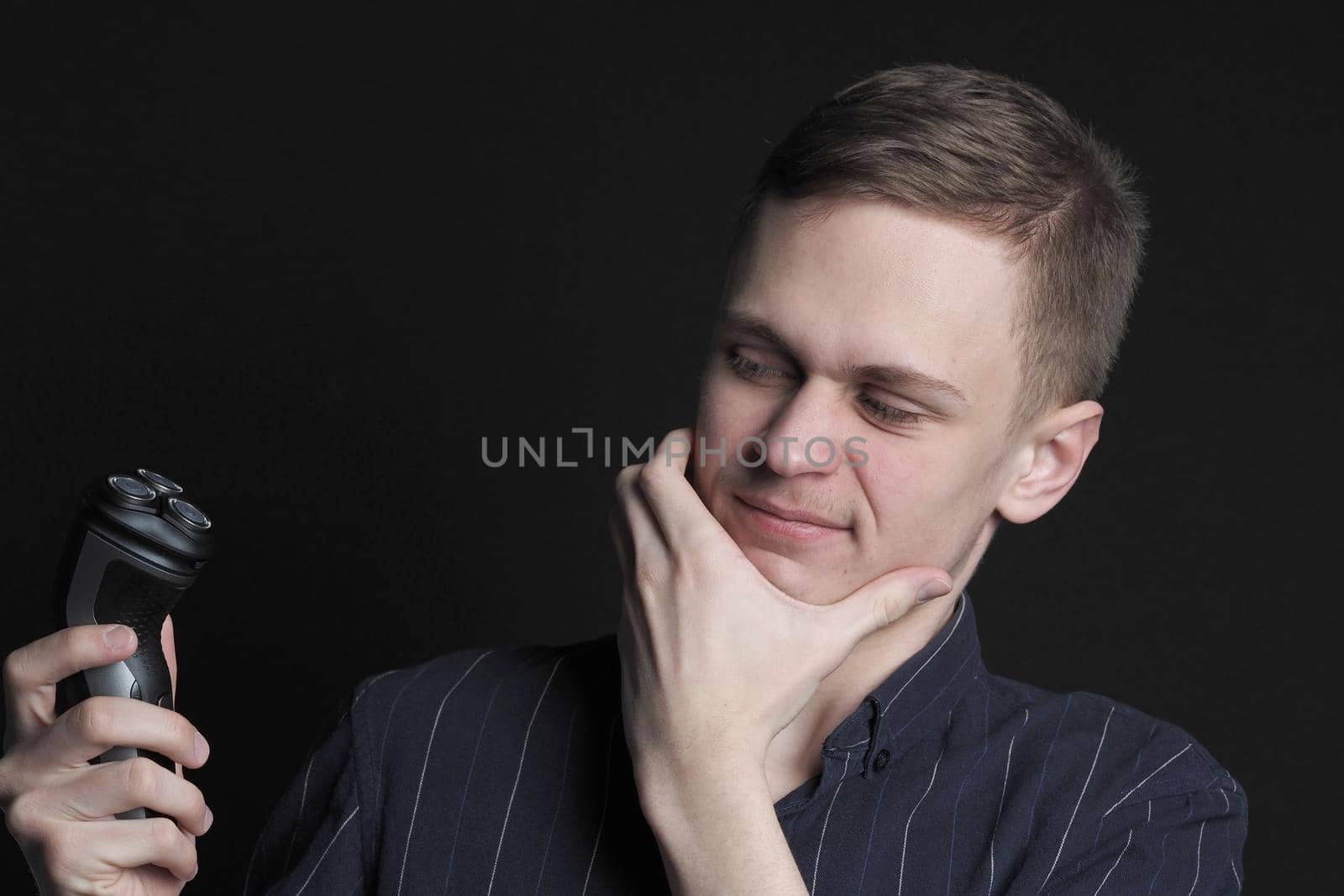 Shave safely. A young man or man of European appearance shaves his face with an electric razor. High quality photo