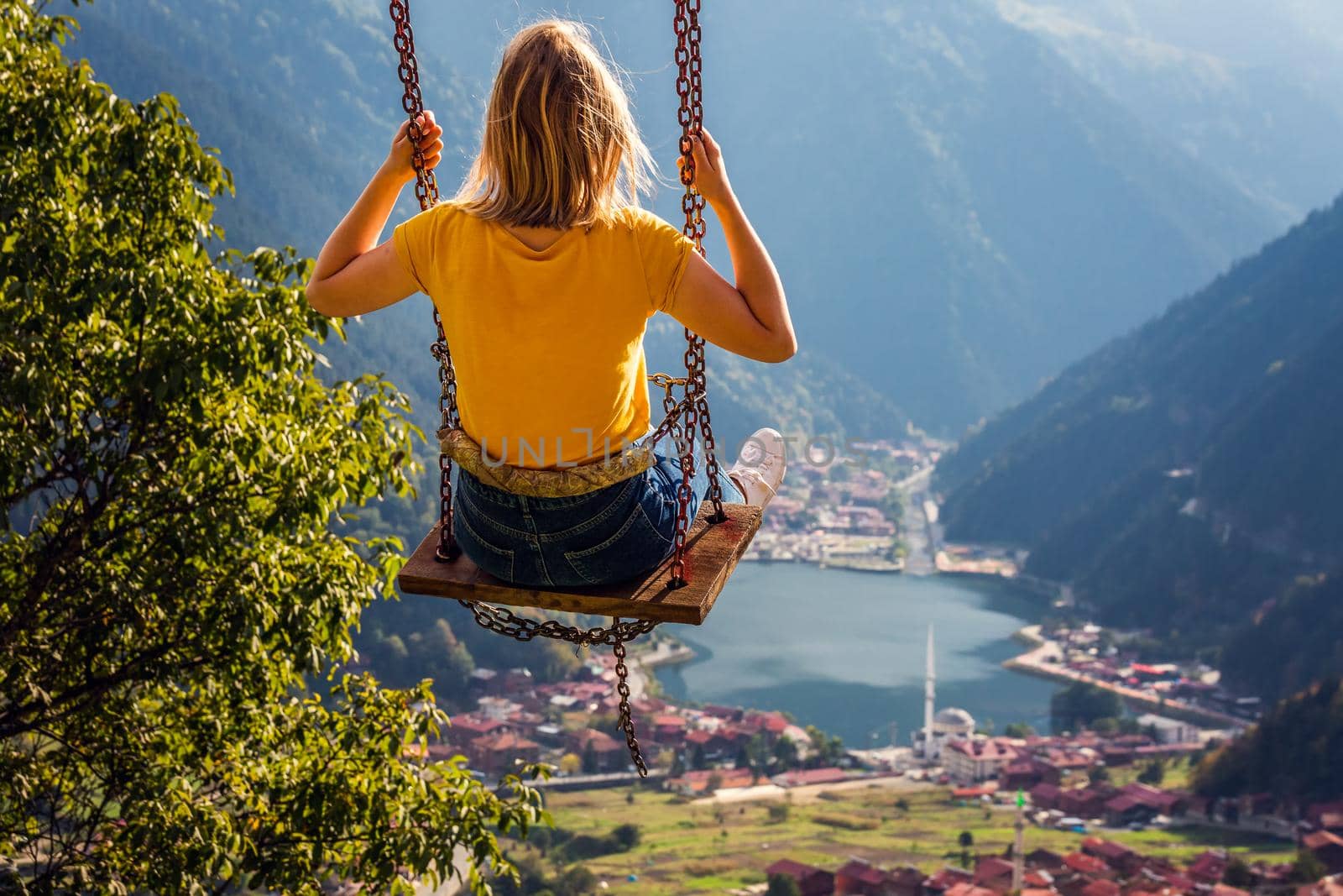 Young female on a swing with the view of the mountain lake Uzungol, Trabzon, Turkey.