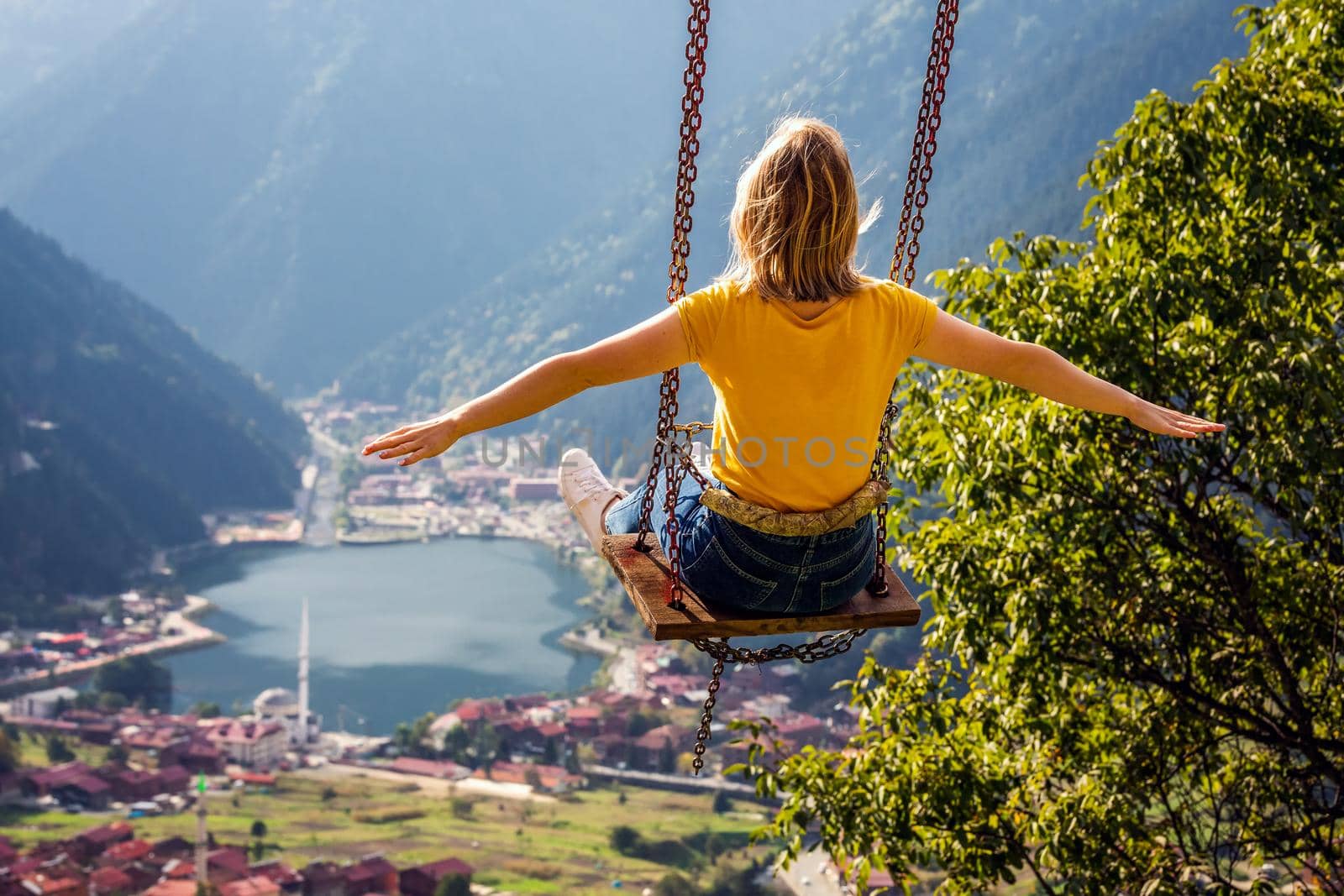 Young female on a swing with the view of the mountain lake Uzungol, Trabzon, Turkey.
