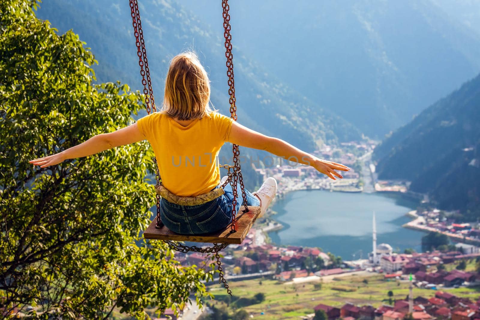 Young female on a swing with the view of the mountain lake Uzungol, Trabzon, Turkey.