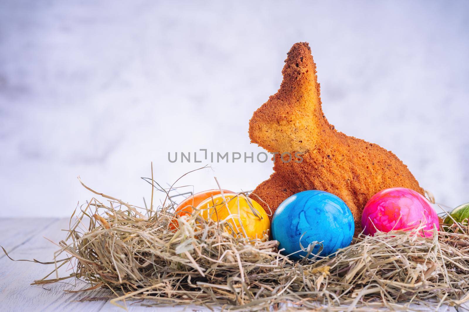 Baked easter bunny cake and easter decorated eggs on straw on wooden background