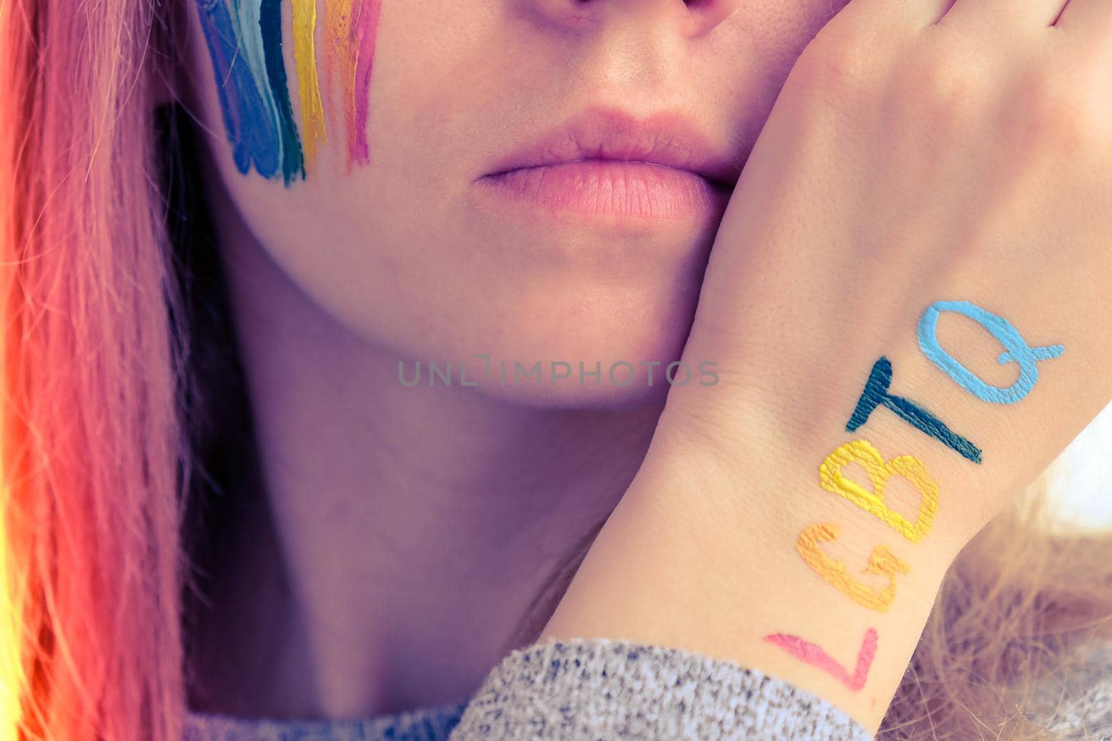 Rainbow LGBTQ flag painted on hand and cheek. Support for lgbt community. Honour of pride month. Connecting people, touching hands. Multi colored hands art creativity, discrimination. Selective focus