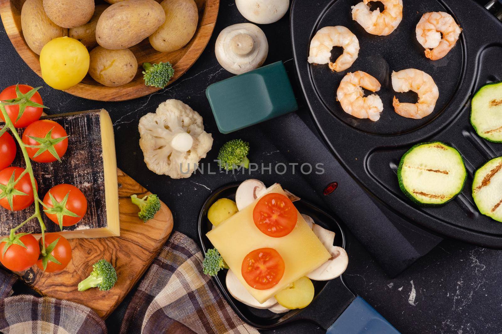 Delicious traditional Swiss melted raclette cheese on chopped boiled potatoes with vegetables.