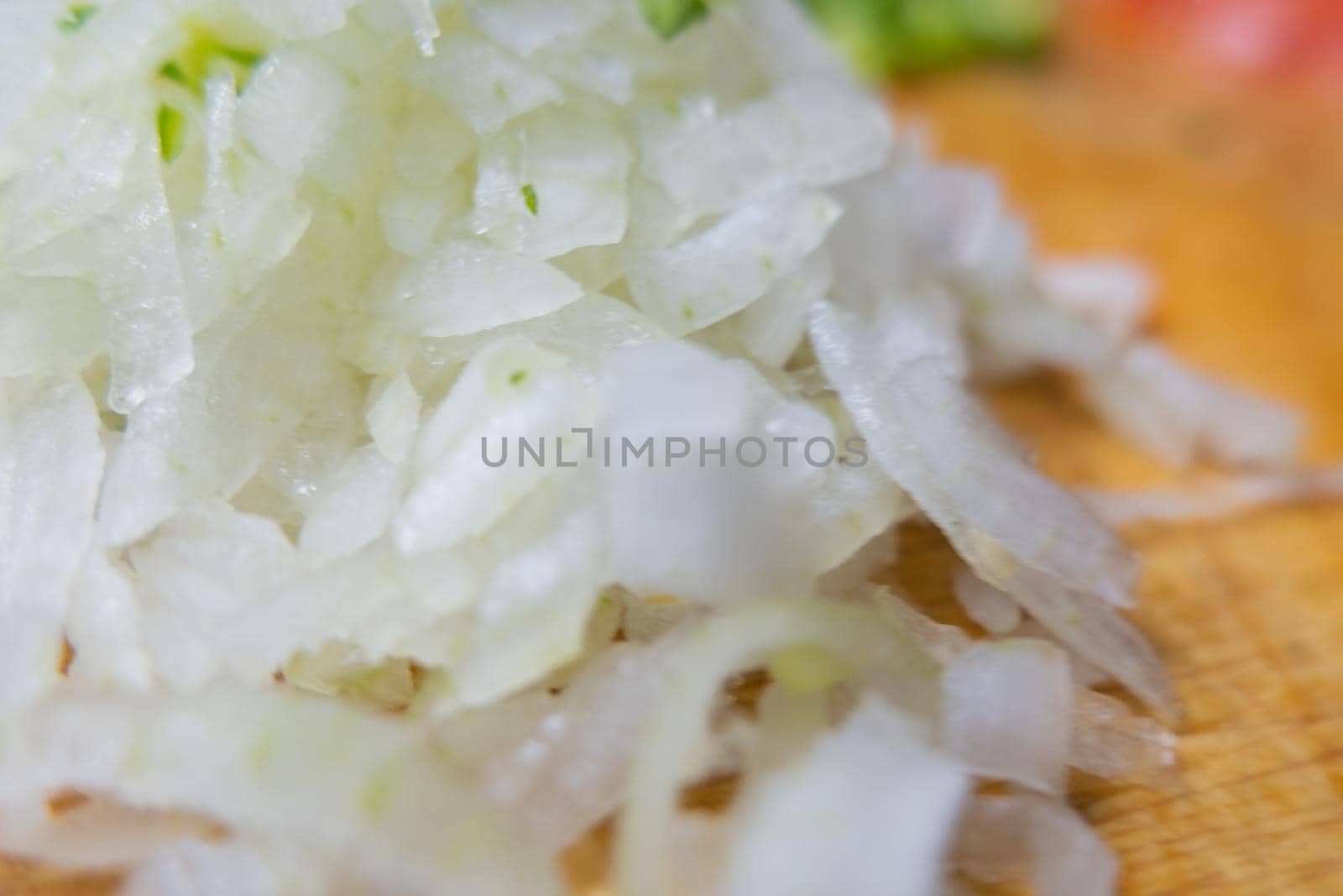 Close-up of chopped onions on wooden cutting board with blurry background. Fresh white vegetables cut into pieces above wood surface. Traditional sauce preparation