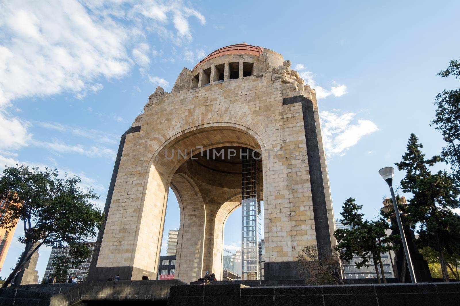 Mexico City, Mexico - January 13, 2021: Low angle view of Monument to the Revolution under a beautiful blue sky. Majestic triumphal arch in Mexico City surrounded by trees. Mexican landmarks