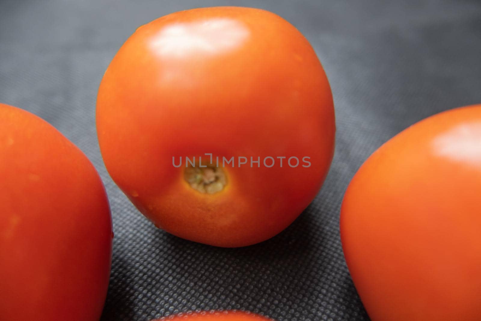 Close-up of three fresh tomatoes on dark blue table. Juicy red vegetables above blue surface up close. Healthy meal preparation