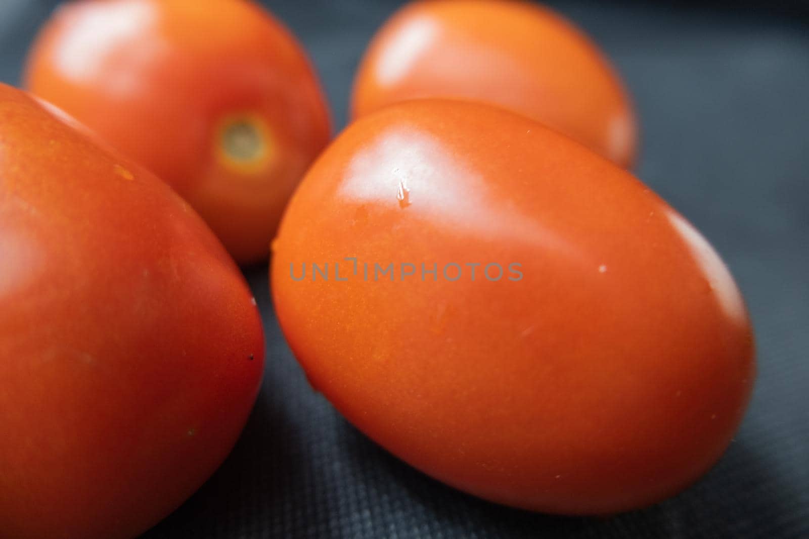 Close-up of four fresh tomatoes on dark blue table. Juicy red vegetables above blue surface up close. Healthy meal preparation