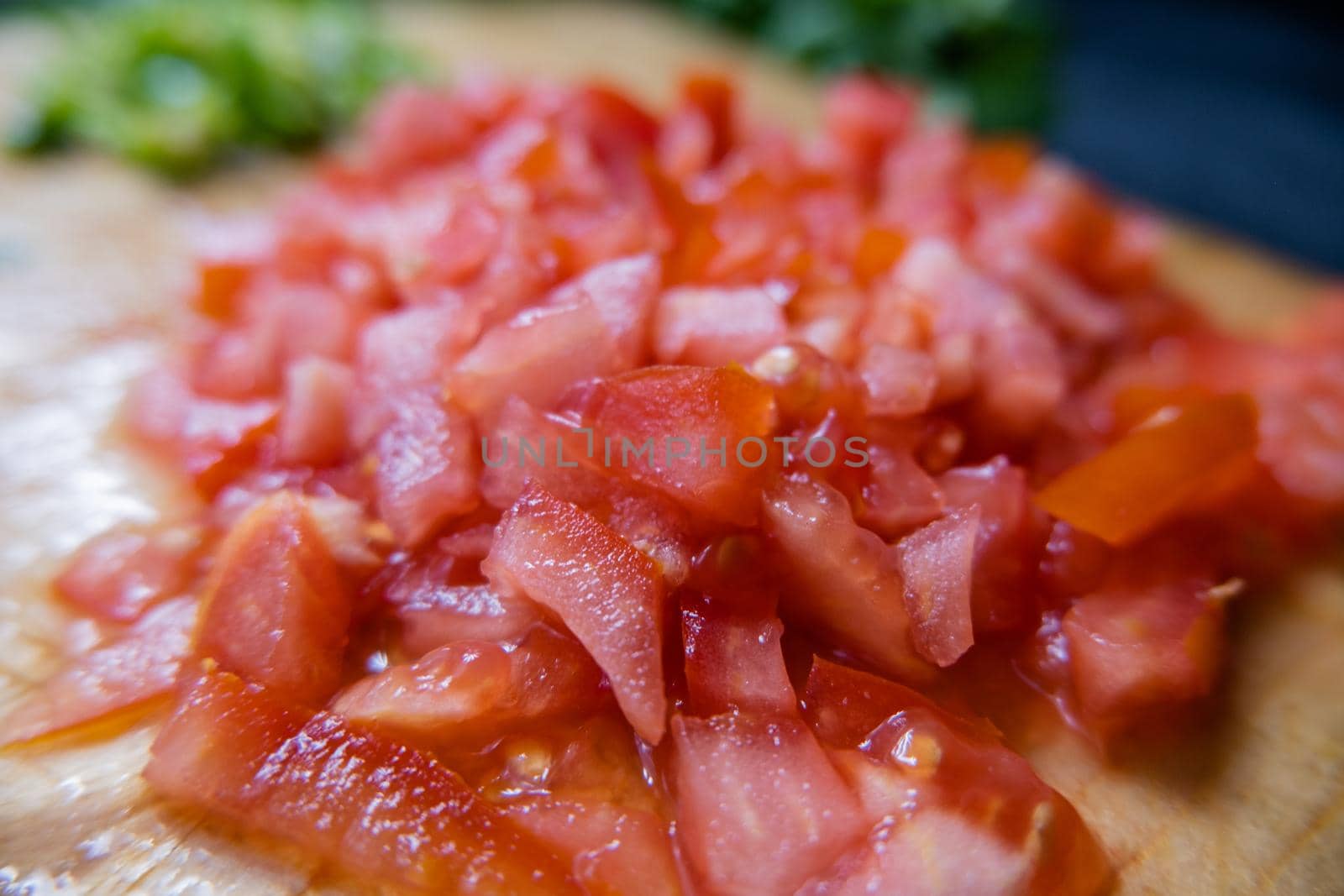 Close-up of fresh chopped tomatoes on wooden cutting table with chili pepper slices as background. Juicy red vegetables cut into pieces above wood surface. Healthy snack preparation