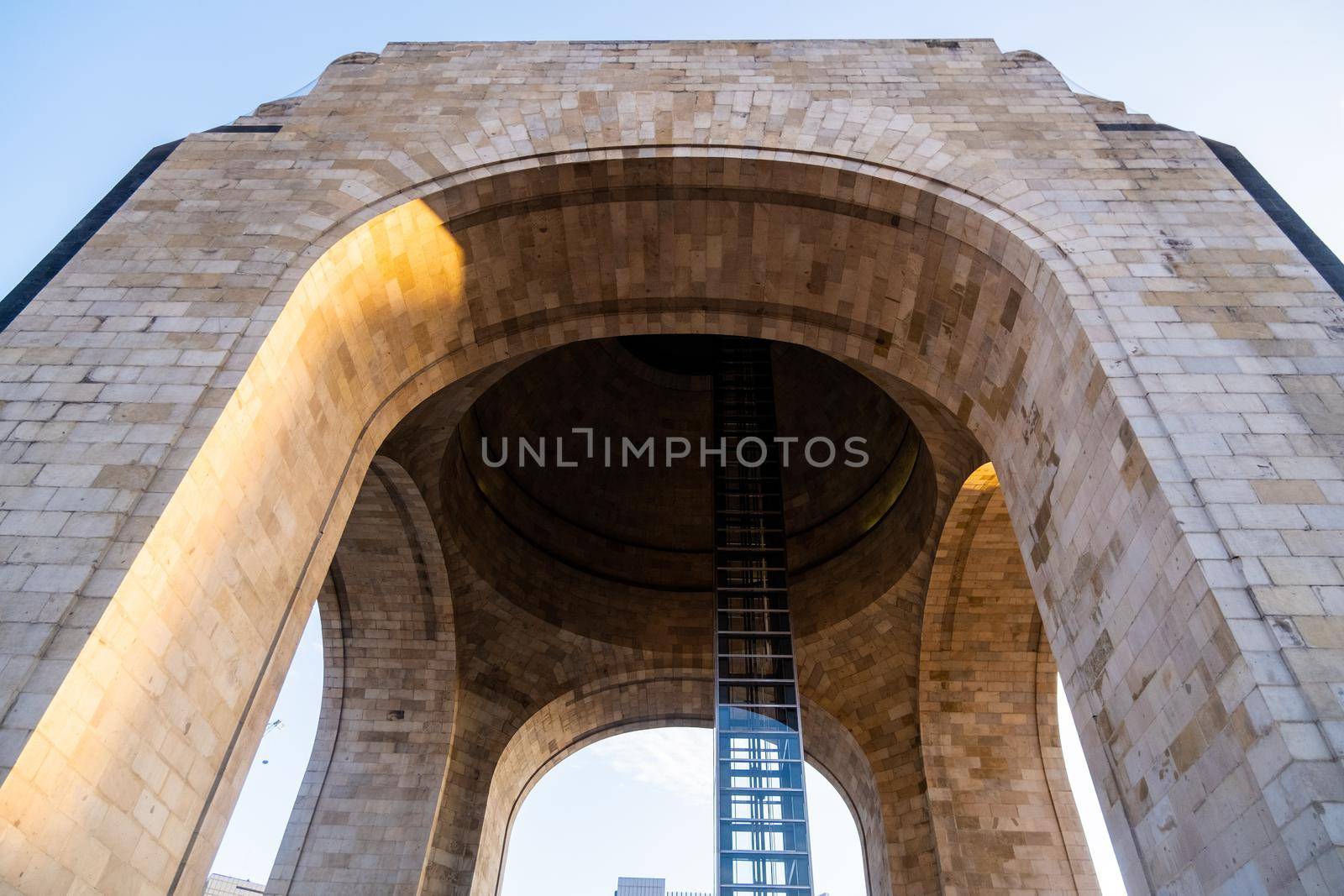 Low angle view of the arch and elevator of the Monument to the Revolution. Majestic triumphal arch in Mexico City with beautiful blue sky as background. Mexican landmarks