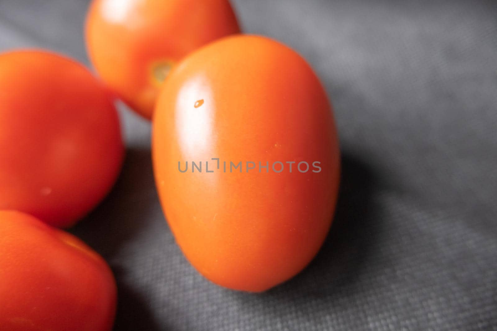 Close-up of four fresh tomatoes on dark blue table. Juicy red vegetables above blue surface up close. Healthy meal preparation