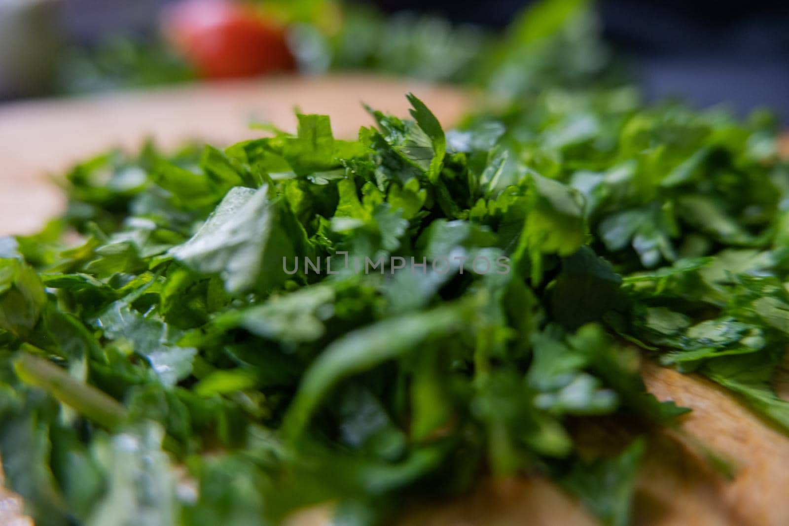 Close-up of freshly chopped coriander on wooden cutting board with blurry background. Fresh green vegetables and herbs cut into pieces above wood surface. Traditional sauce preparation