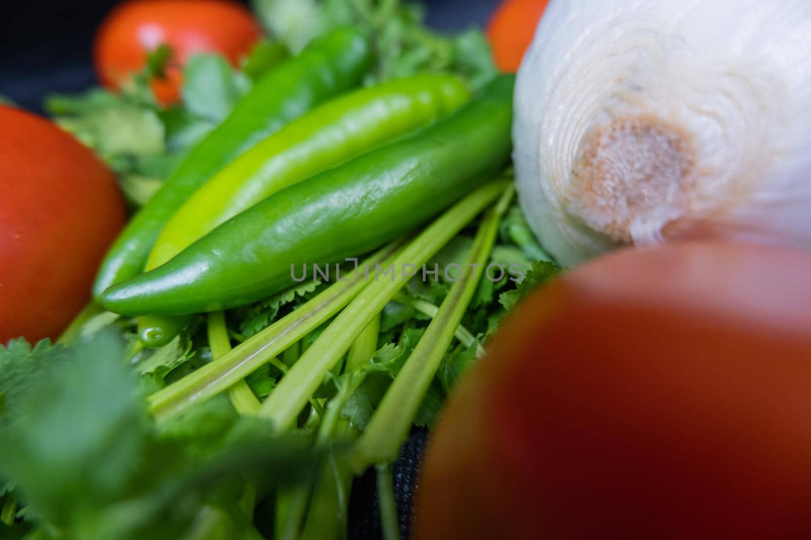 Close-up of three green chili peppers, onion, and tomato above coriander. Fresh and aromatic green, white, and red vegetables up close. Healthy meal preparation