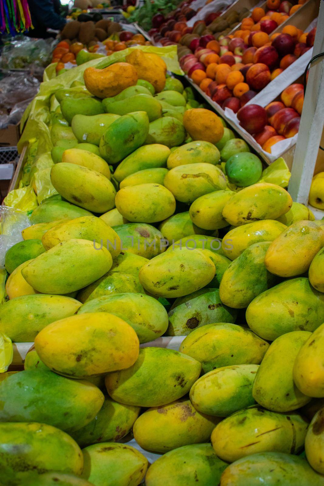 Colorful and unripe mangoes, peaches, and more fruit for sale. Variety of fresh fruit displayed in stand inside Mexican market. Healthy eating