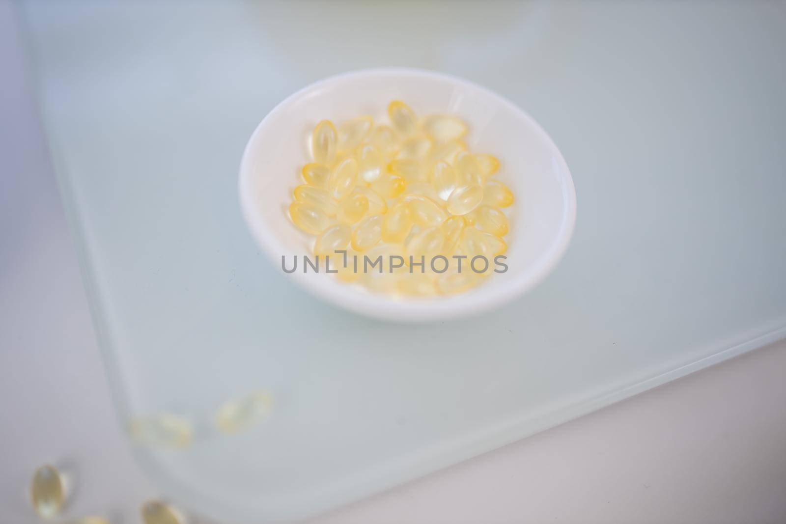 Close-up of small bowl of vitamin C pills on transparent cutting board. Transparent capsules in porcelain bowl above white surface. Vitamin C nutrition