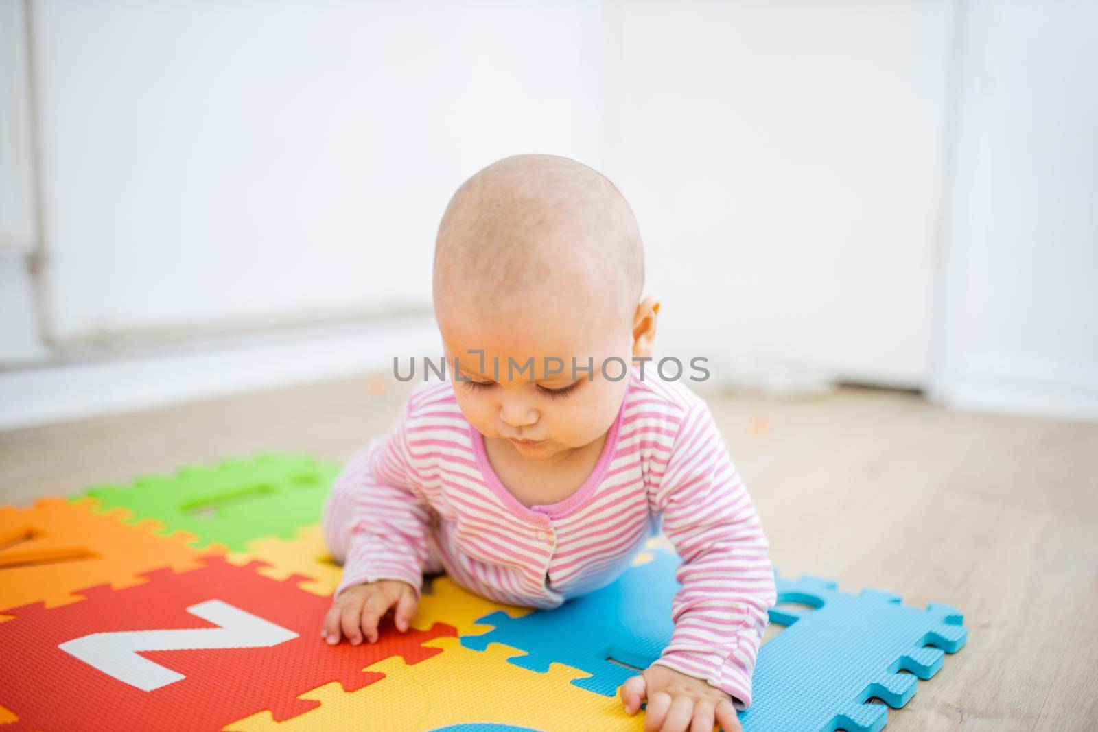 Adorable baby lying on a colorful mat with letters by Kanelbulle