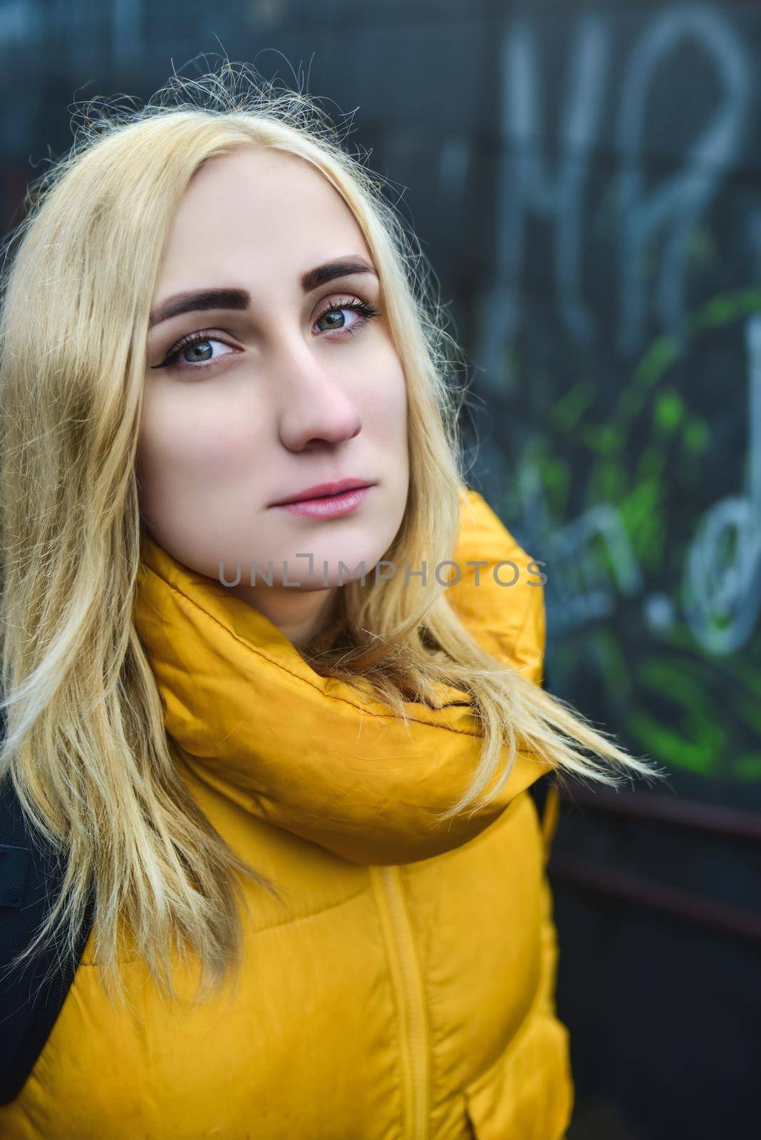 Close up portrait of blonde hipster teen girl making selfie, She is wearing yellow jacket and backpack, walking outdoors throught underground passage by Nickstock