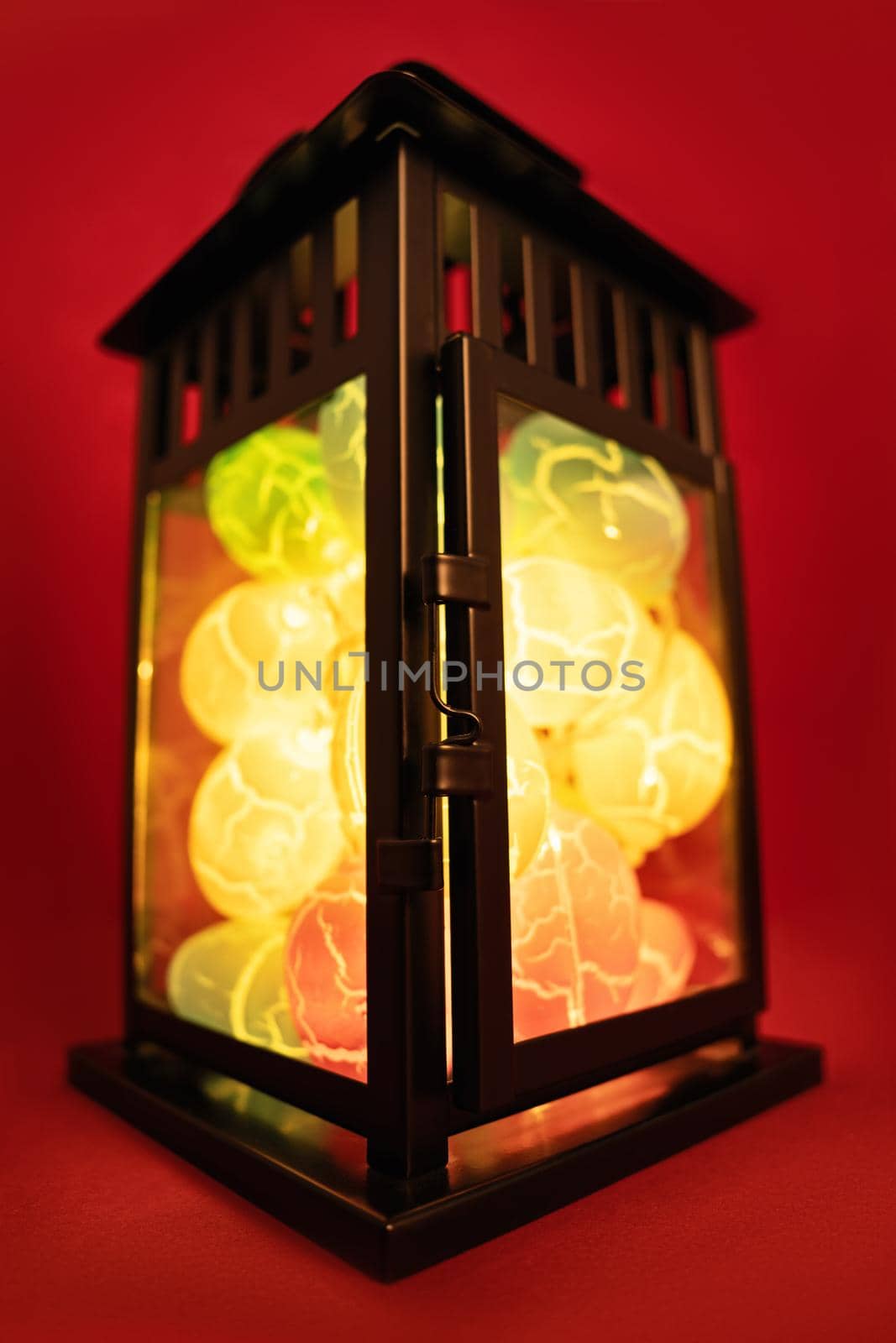 Close up of Easter egg shaped lights in a black lantern, on red background. Easter decoration concept. Fun and colorful Easter celebration concept.