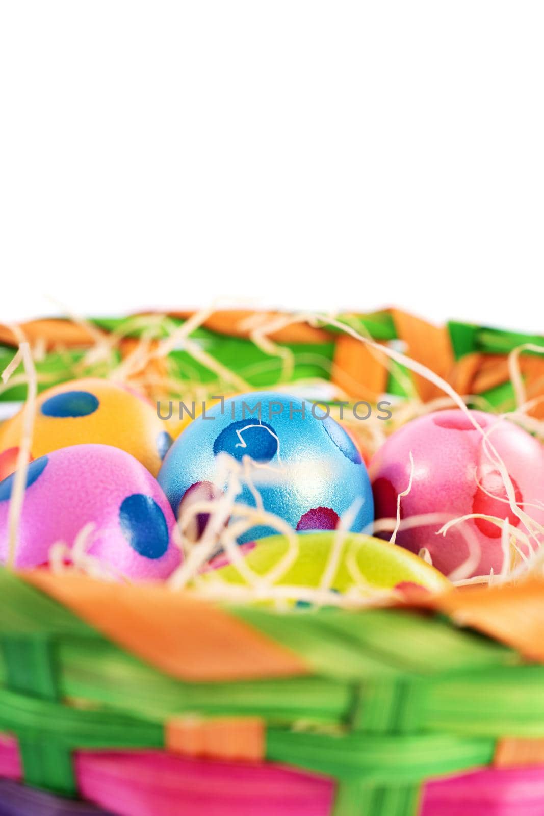 Close up of colourful Easter eggs with polka dots in a basket, isolated on white background. Easter celebration concept.