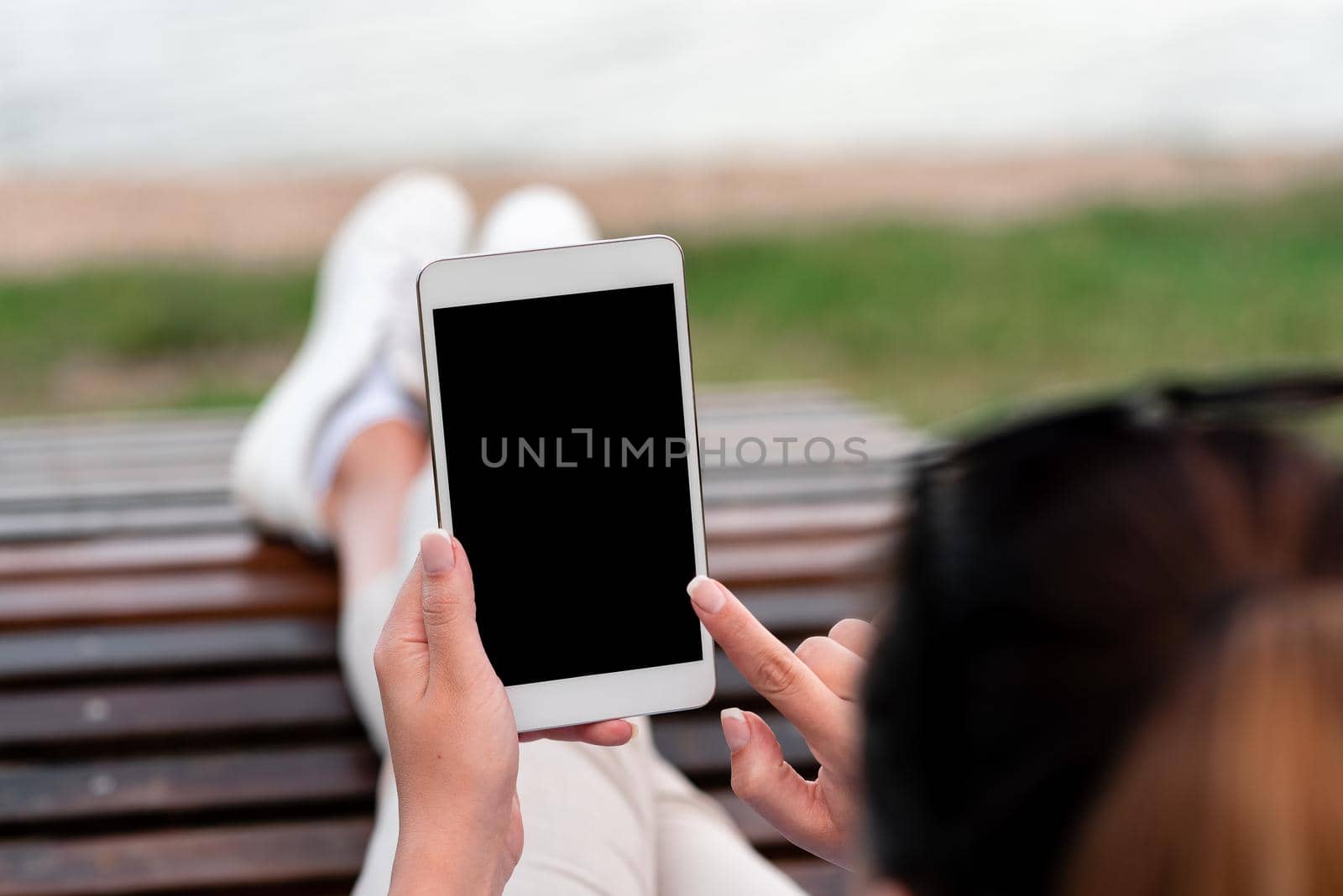 Top view mockup image of woman's hands holding and using black tablet pc with blank white desktop screen while sitting on the floor.