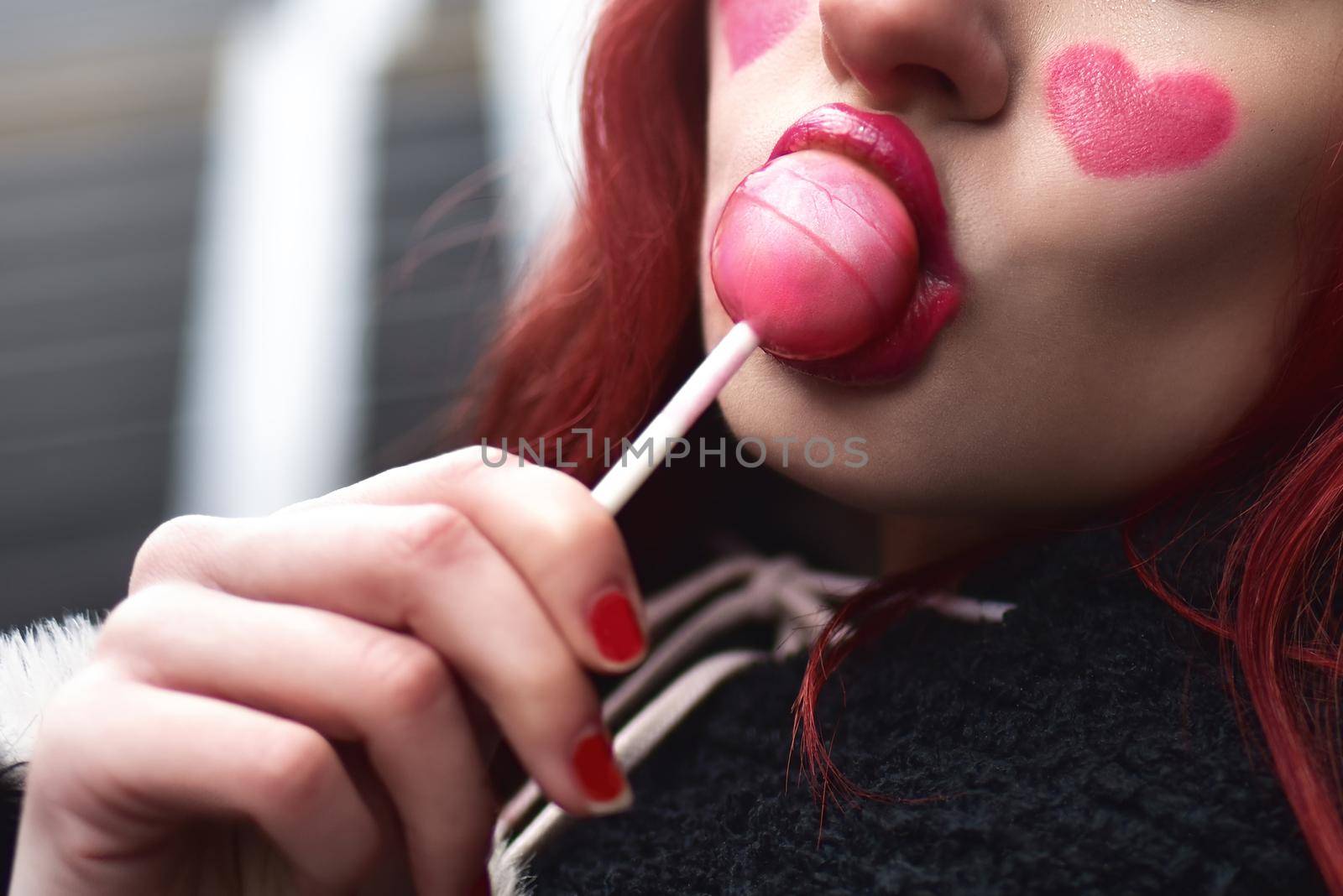 Glamorous photo with sexy female lips licking a strawberry lollipop. Beautiful daring bright fashionable makeup.