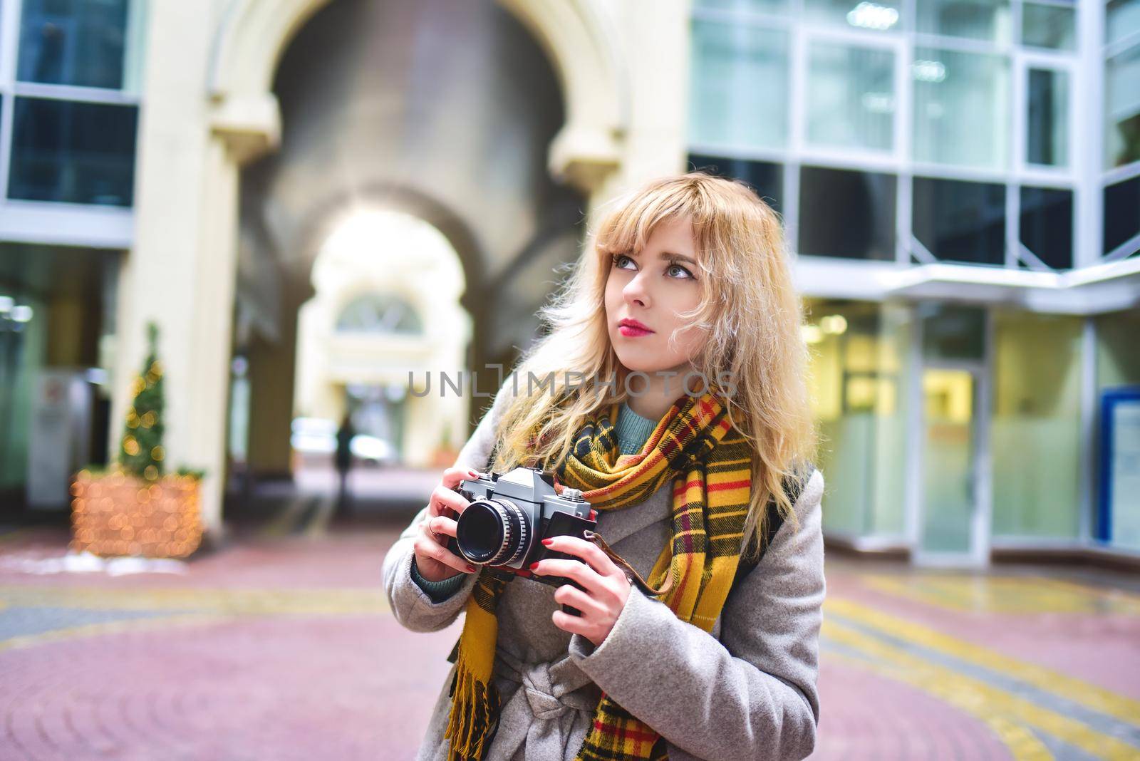 Blonde pretty photographer woman with retro camera in her hands while taking shots at urban old architecture. Discover new places. by Nickstock