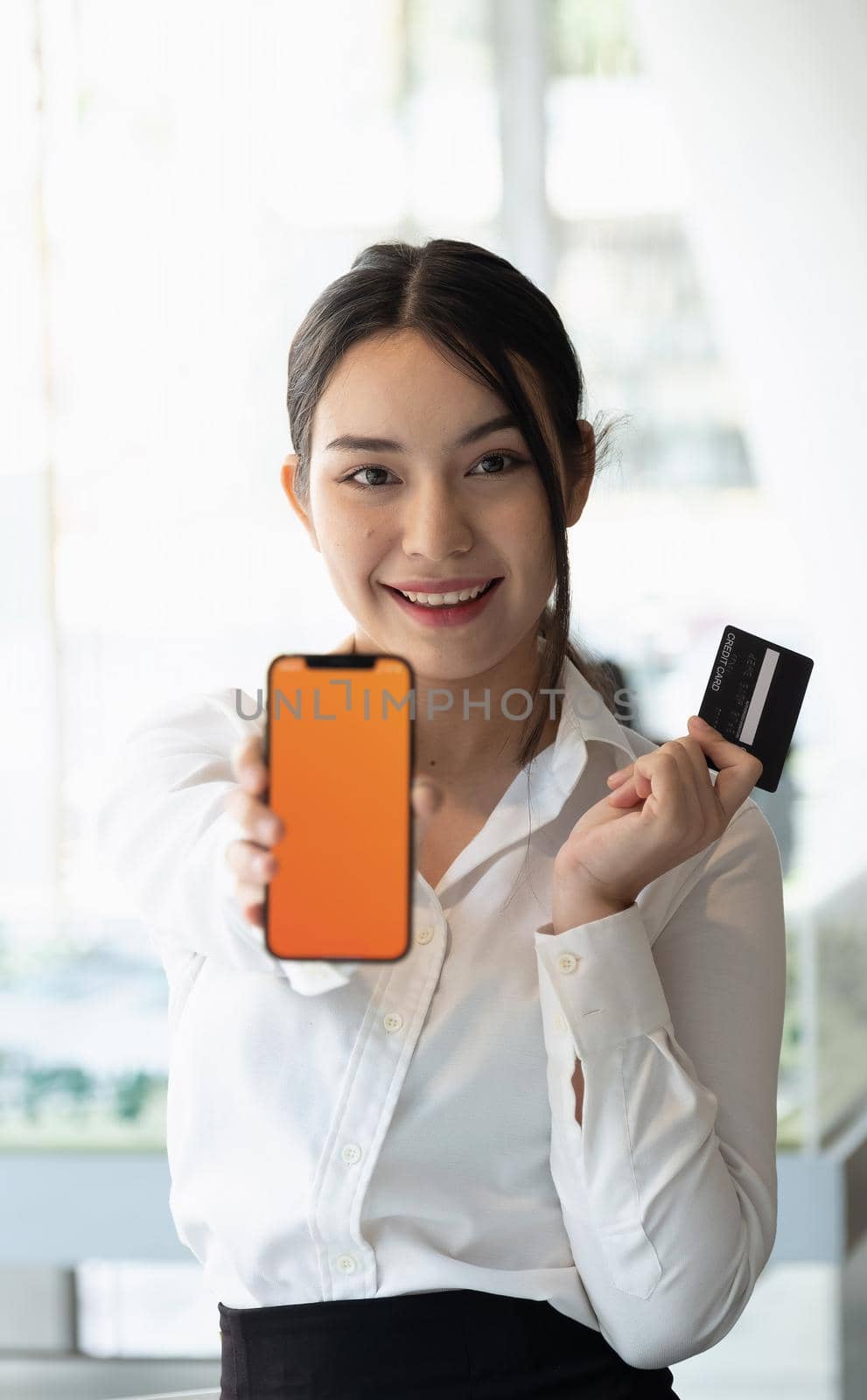 Portrait of smiling young woman show smartphone and credit card for shopping online at home
