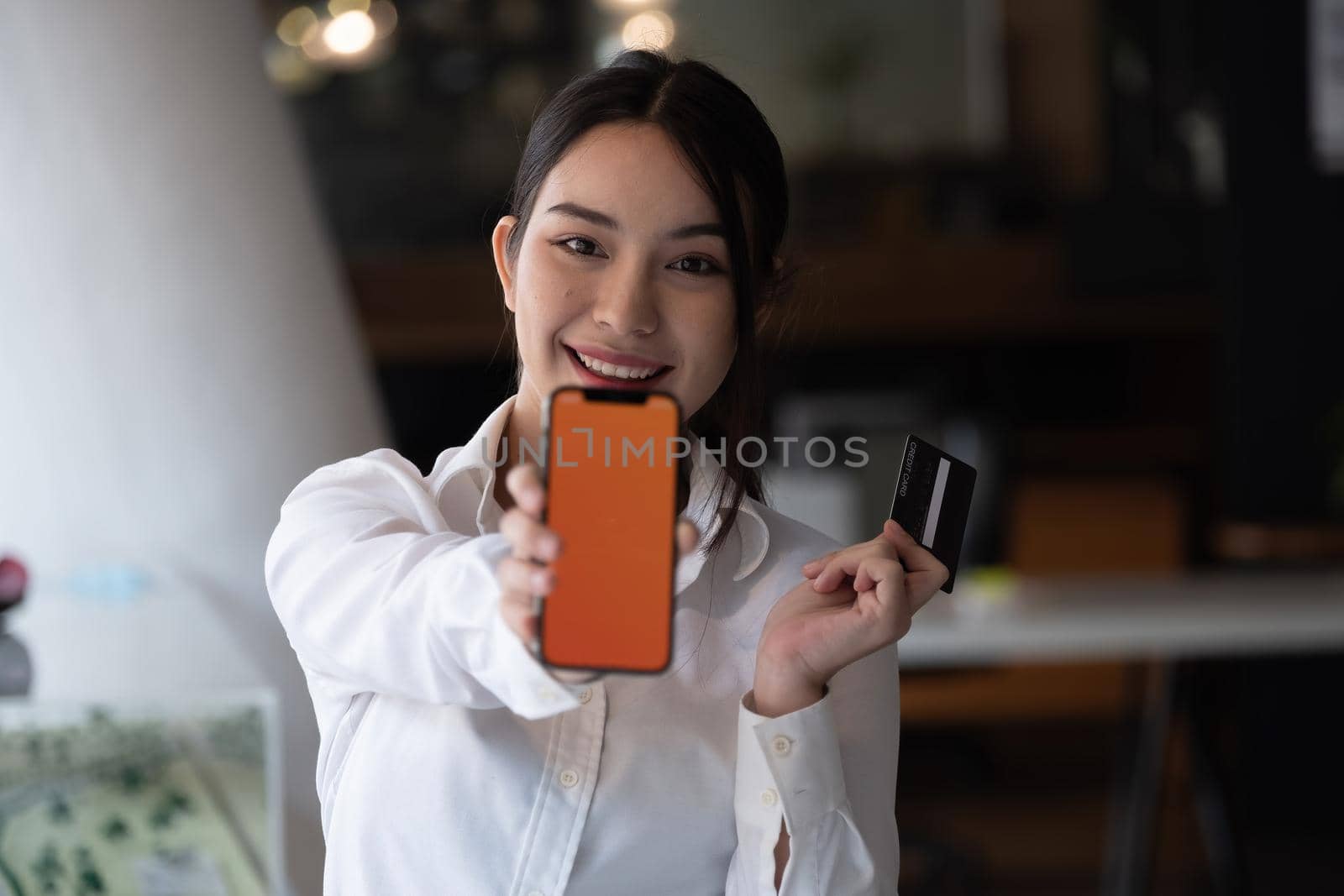 Portrait of smiling young woman show smartphone and credit card for shopping online at home. by nateemee