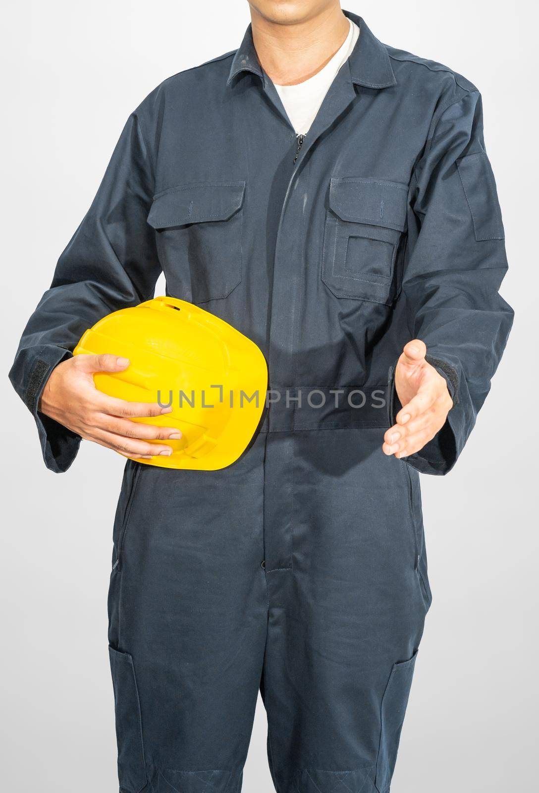 Worker standing in blue coverall holding yellow hardhat isolated on gray background