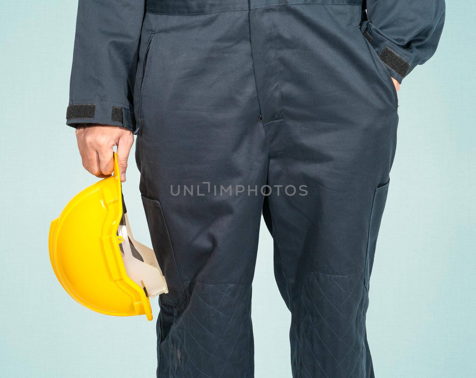 Worker standing in blue coverall holding yellow hardhat isolated on blue background