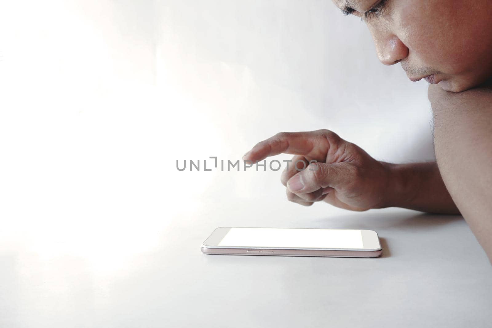 Selective focus image of face male hands using smartphone at home on a white room, searching or social chat networks concept.
