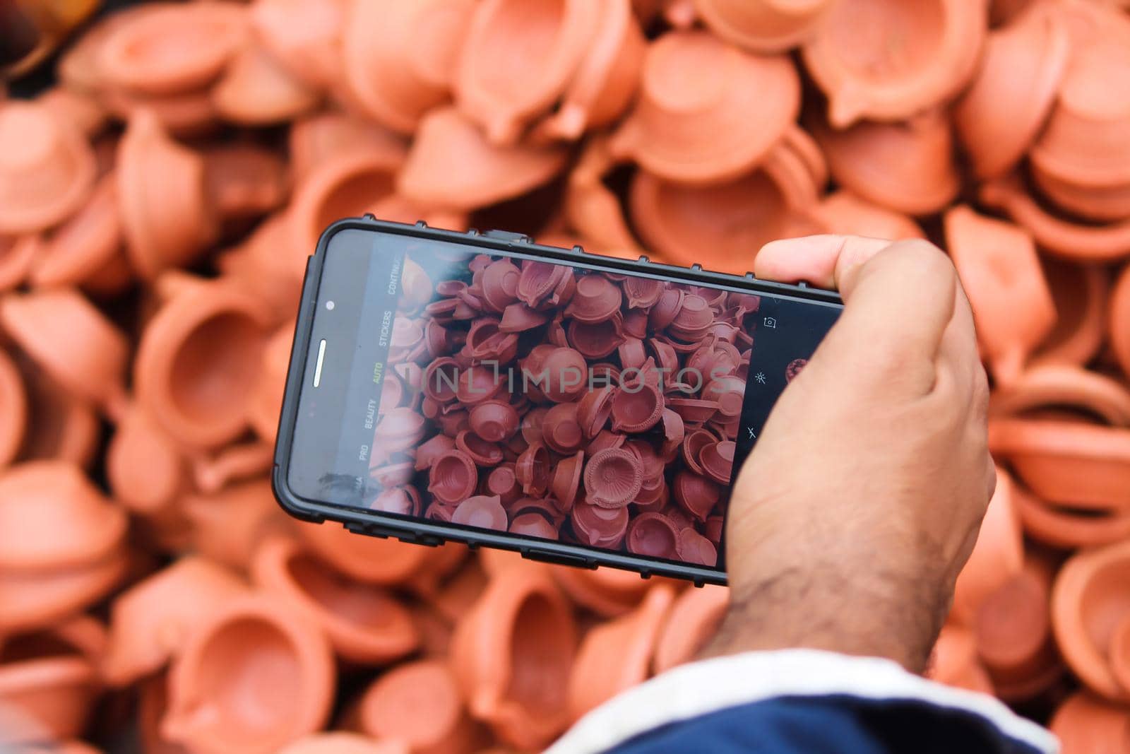 Man taking photos of clay lamps (Diya) with his phone at a market in India for the festival of Diwali