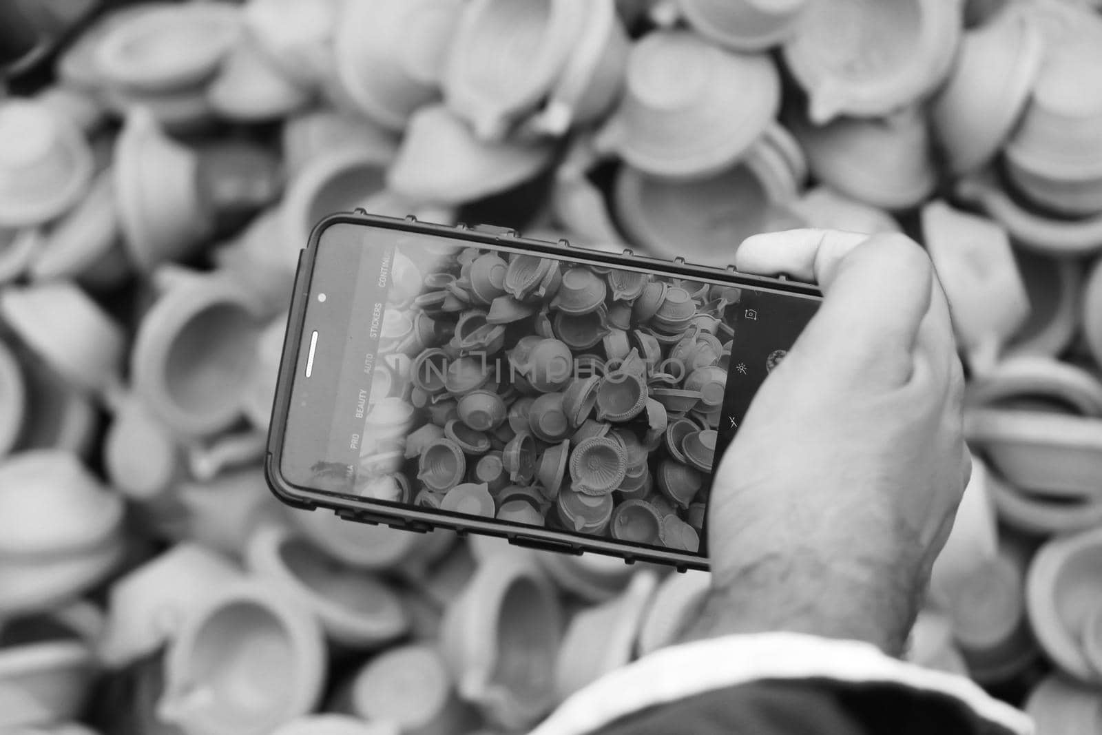 Black and White image of Man taking photos of clay lamps (Diya) with his phone at a market in India for the festival of Diwali