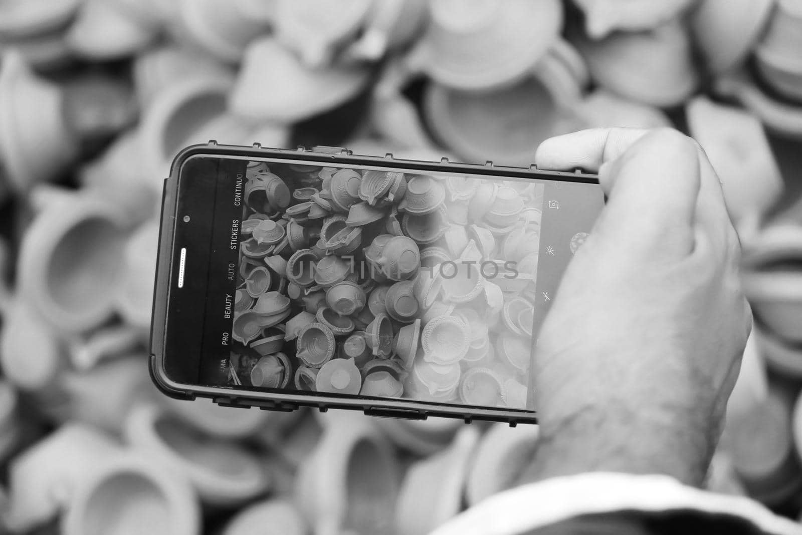 Black and White image of Man taking photos of clay lamps (Diya) with his phone at a market in India for the festival of Diwali by tabishere