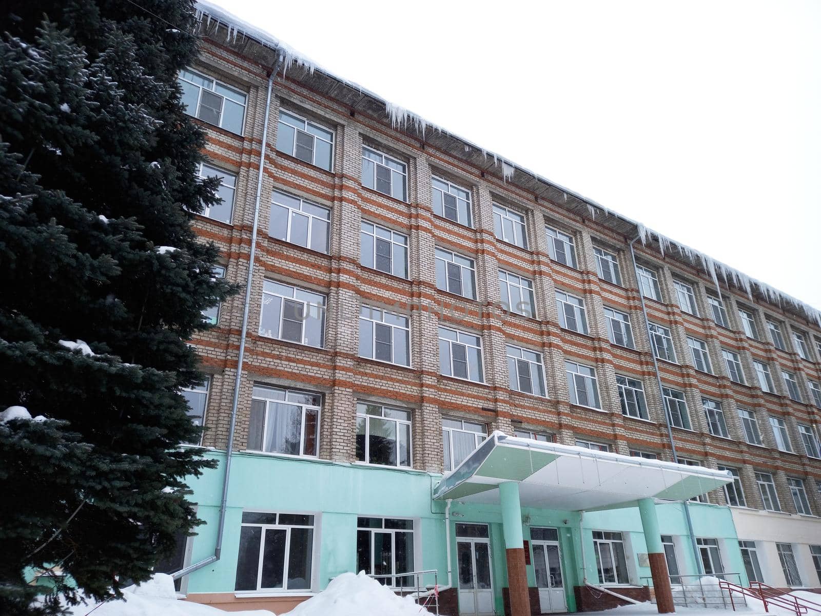 A large brick house or administrative building in winter. Icicles hang from the roof. High quality photo