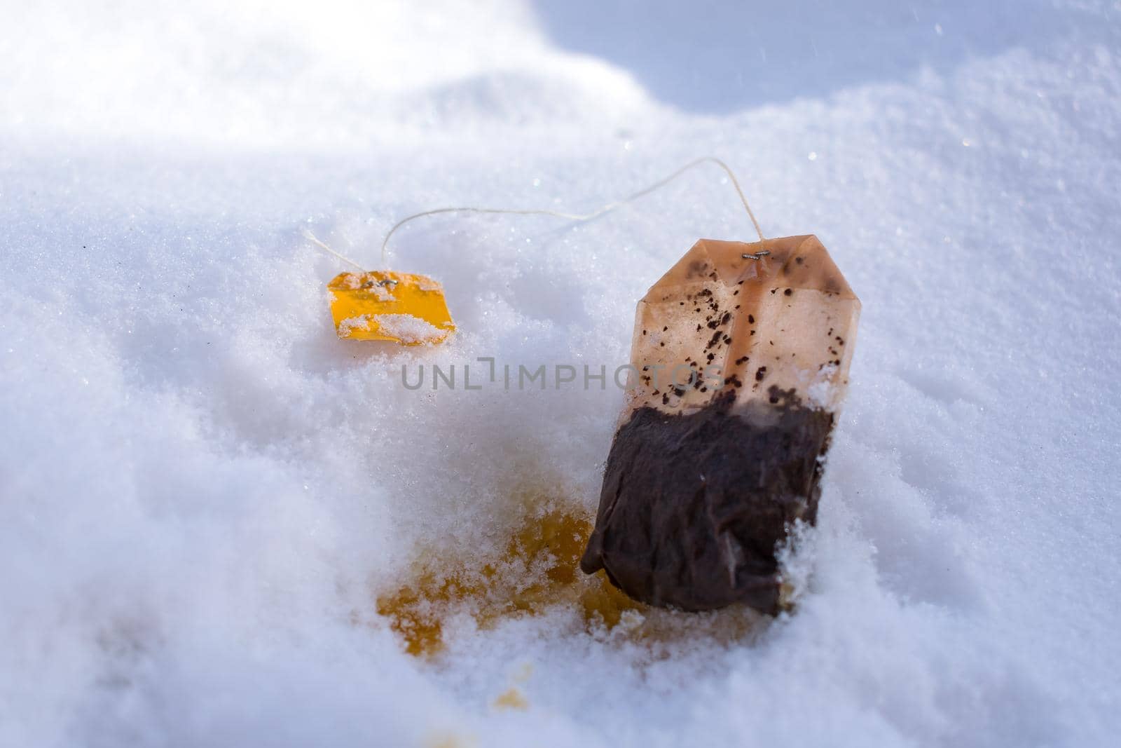 A used tea bag lies in the snow like rubbish and pollutes the environment