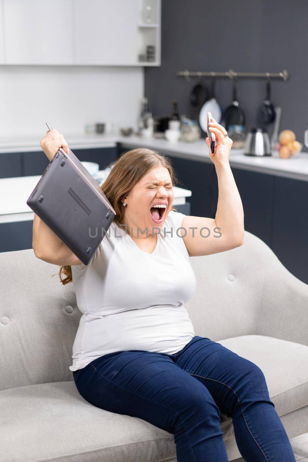 Fury, rage, anger with laptop in hand young overweight girl staying at home during quarantine. Self isolation as prevention. Work distantly concept. Facial expressions, emotions, feelings by LipikStockMedia