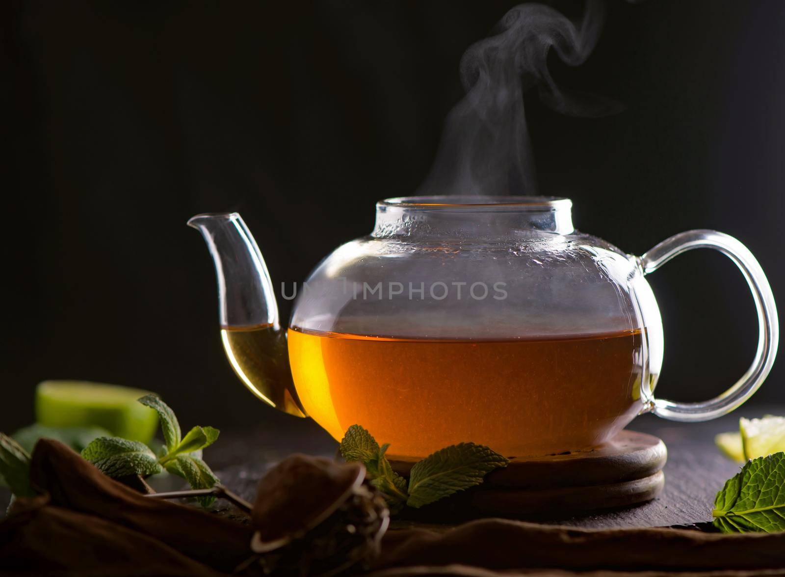 Teapot with tea surrounded with green leaves, tea ceremony, green tea in a transparent cup