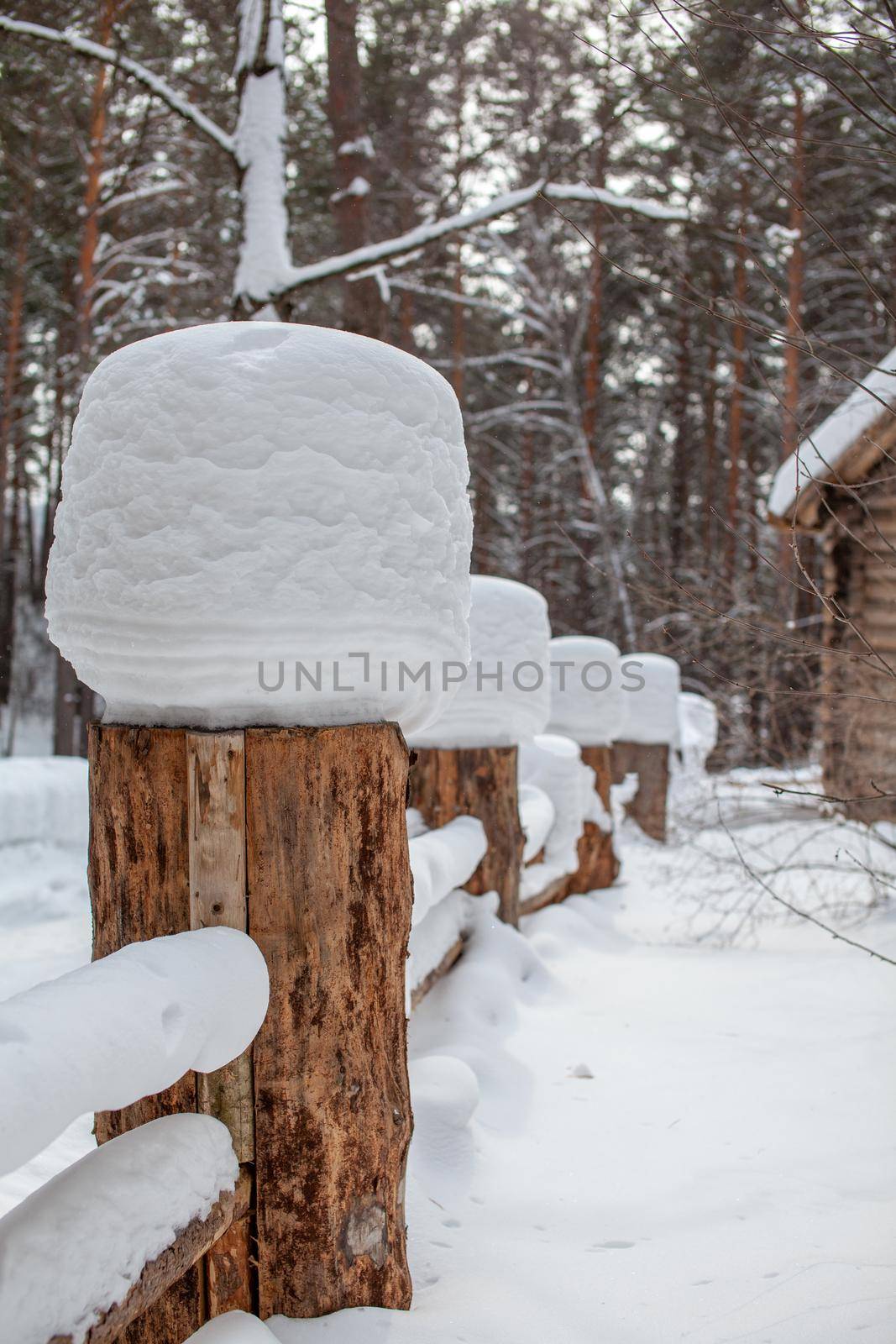 Large snow caps on the stumps of the fence in winter. A wooden fence protects the territory of the house.