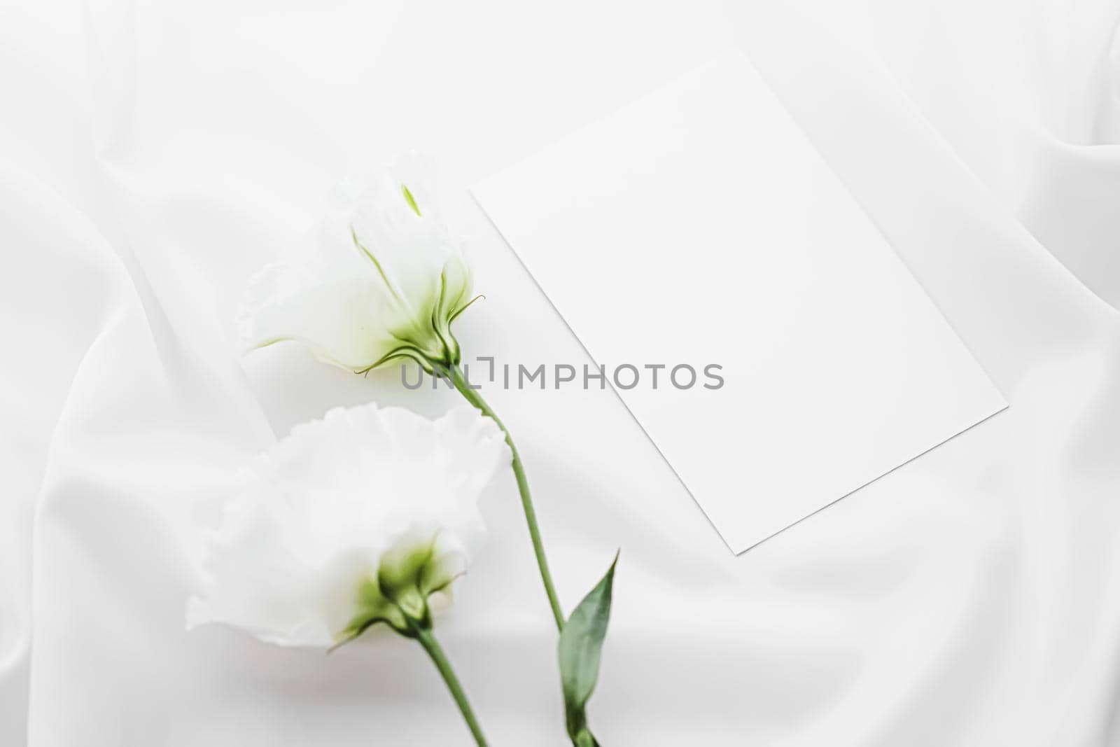 Wedding invitation and white rose flowers on silk fabric as bridal flatlay background, blank paper greeting card and holiday branding, flat lay design concept