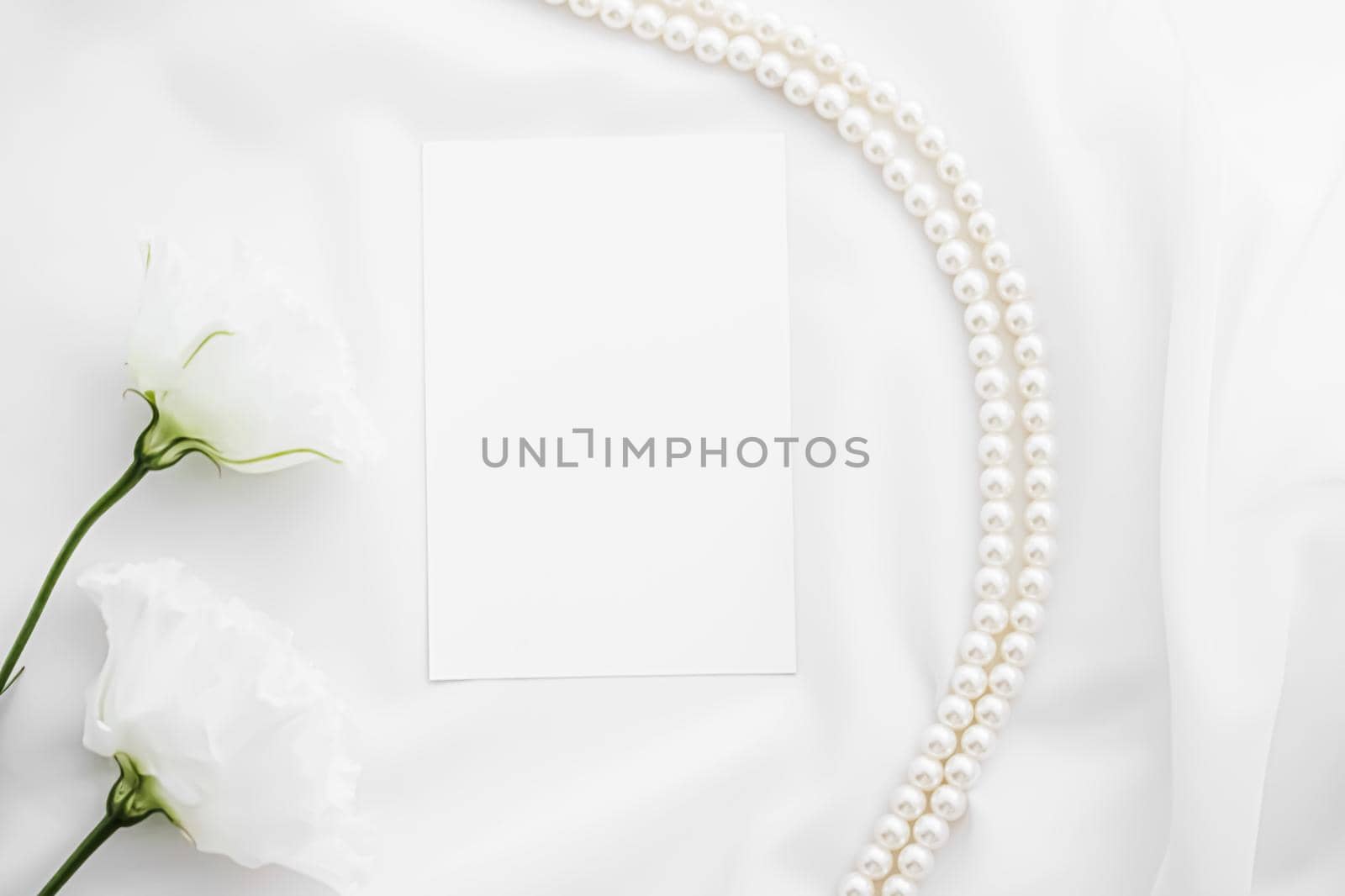 Wedding invitation, white rose flowers and pearls on silk fabric as bridal flatlay background, blank paper greeting card and holiday branding, flat lay design concept