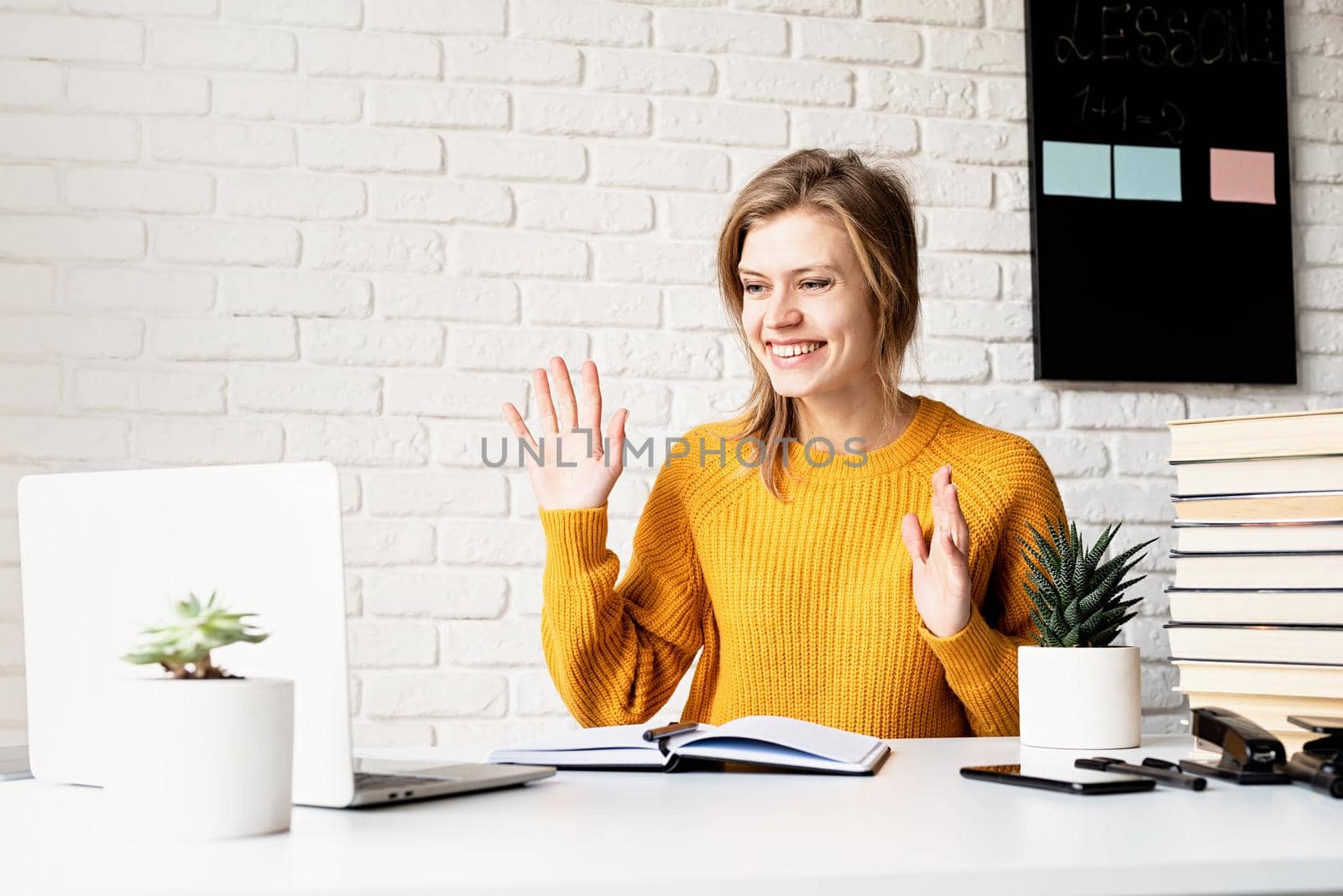 Young smiling woman in yellow sweater studying online using laptop by Desperada