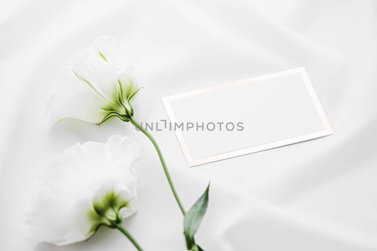 Wedding invitation or gift card and white rose flowers on silk fabric as bridal flatlay background, blank paper and holiday branding, flat lay design concept