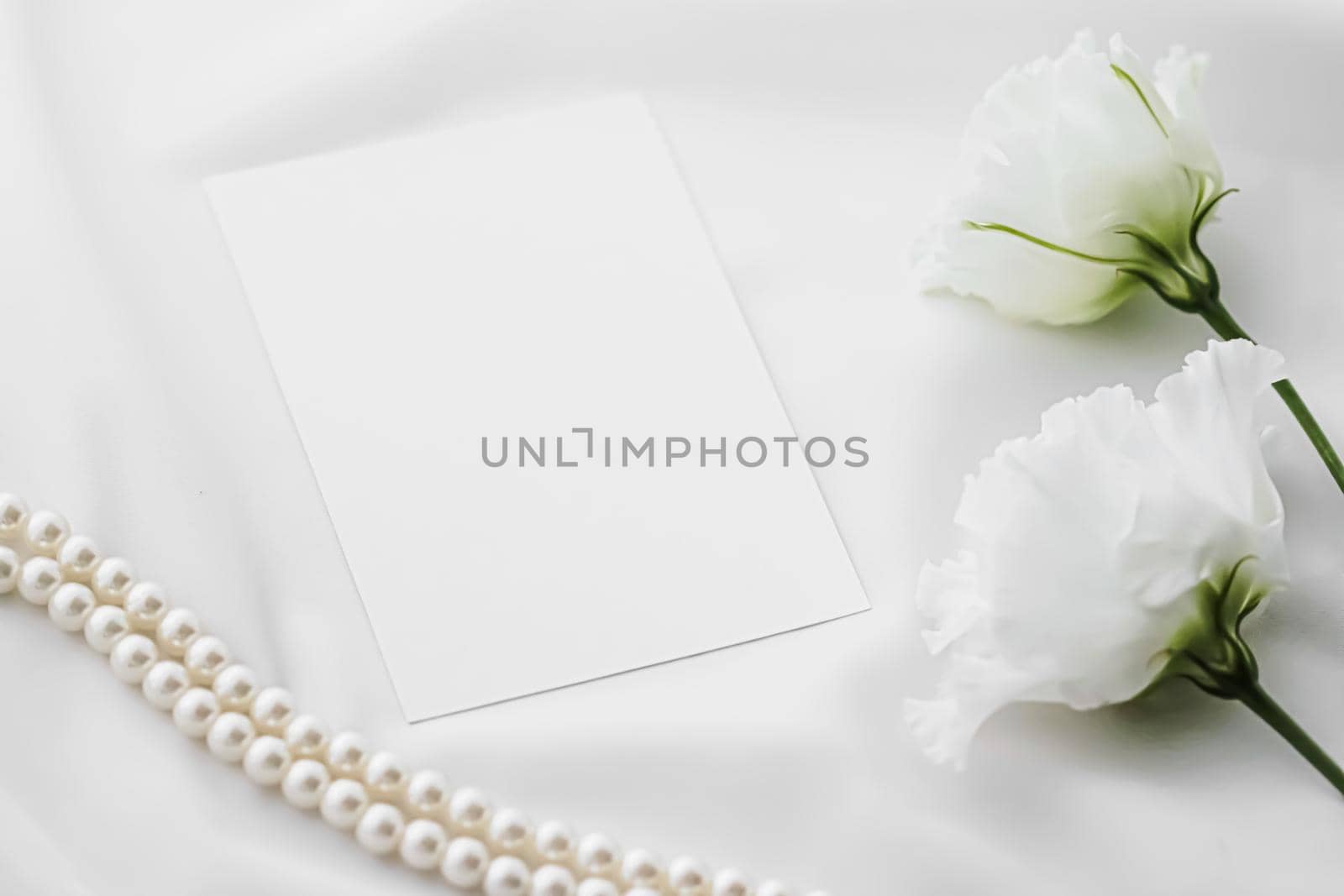 Wedding invitation, white rose flowers and pearls on silk fabric as bridal flatlay background, blank paper greeting card and holiday branding, flat lay design concept