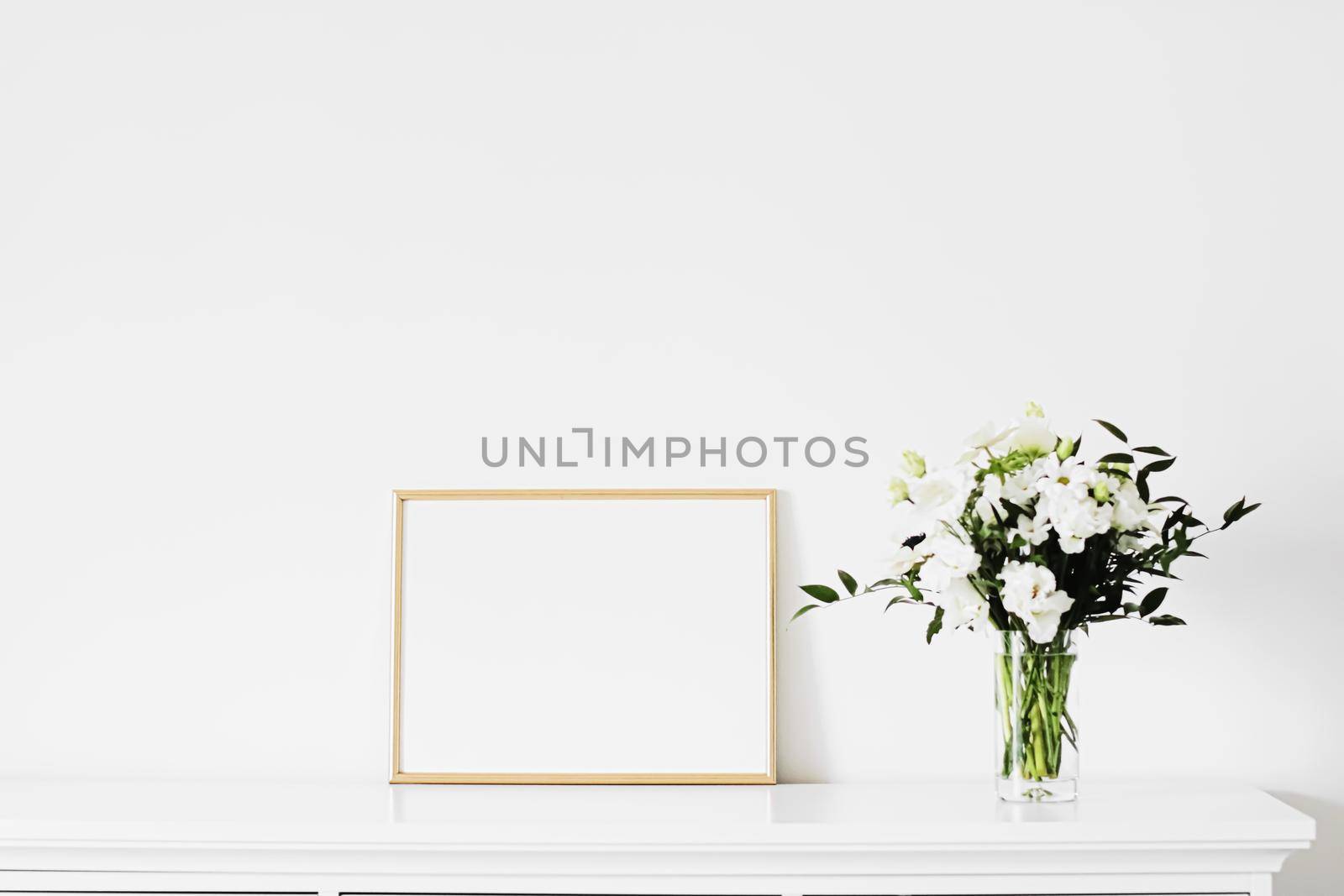 Golden horizontal frame and bouquet of fresh flowers on white furniture, luxury home decor and design for mockup creation by Anneleven