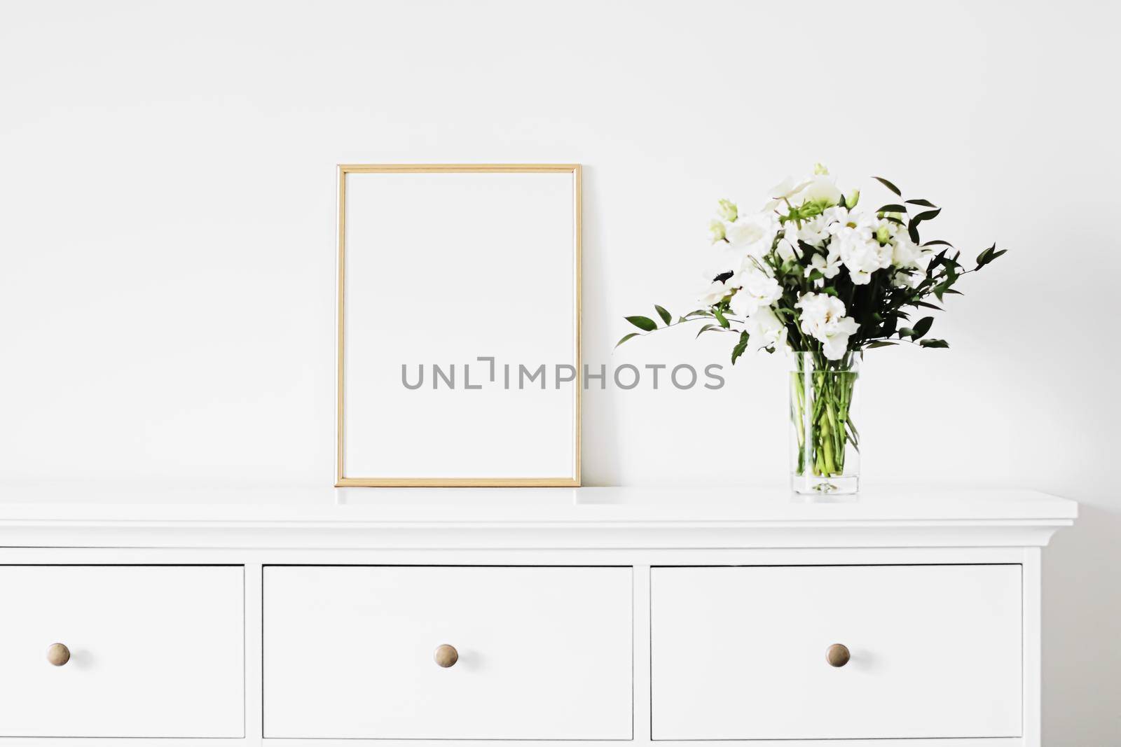 Golden vertical frame and bouquet of fresh flowers on white furniture, luxury home decor and design for mockup creation by Anneleven