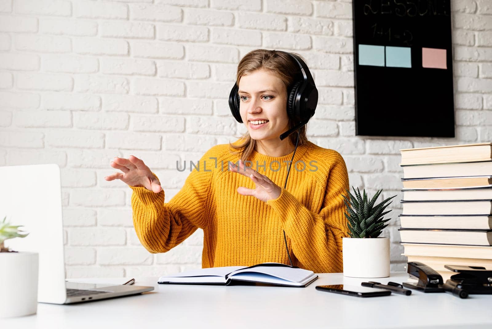 Distance learning. E-learning. Young smiling woman in yellow sweater and black headphones studying online using laptop talking in video chat