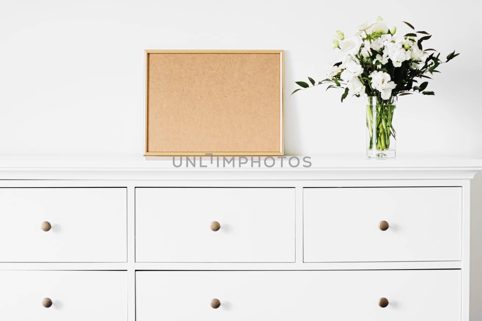 Golden horizontal frame and bouquet of fresh flowers on white furniture, luxury home decor and design for mockup creations