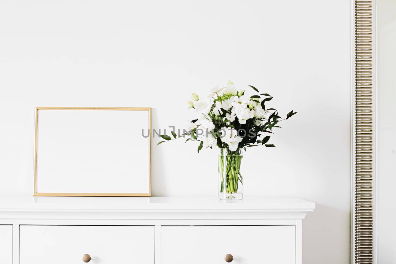 Golden horizontal frame and bouquet of fresh flowers on white furniture, luxury home decor and design for mockup creations