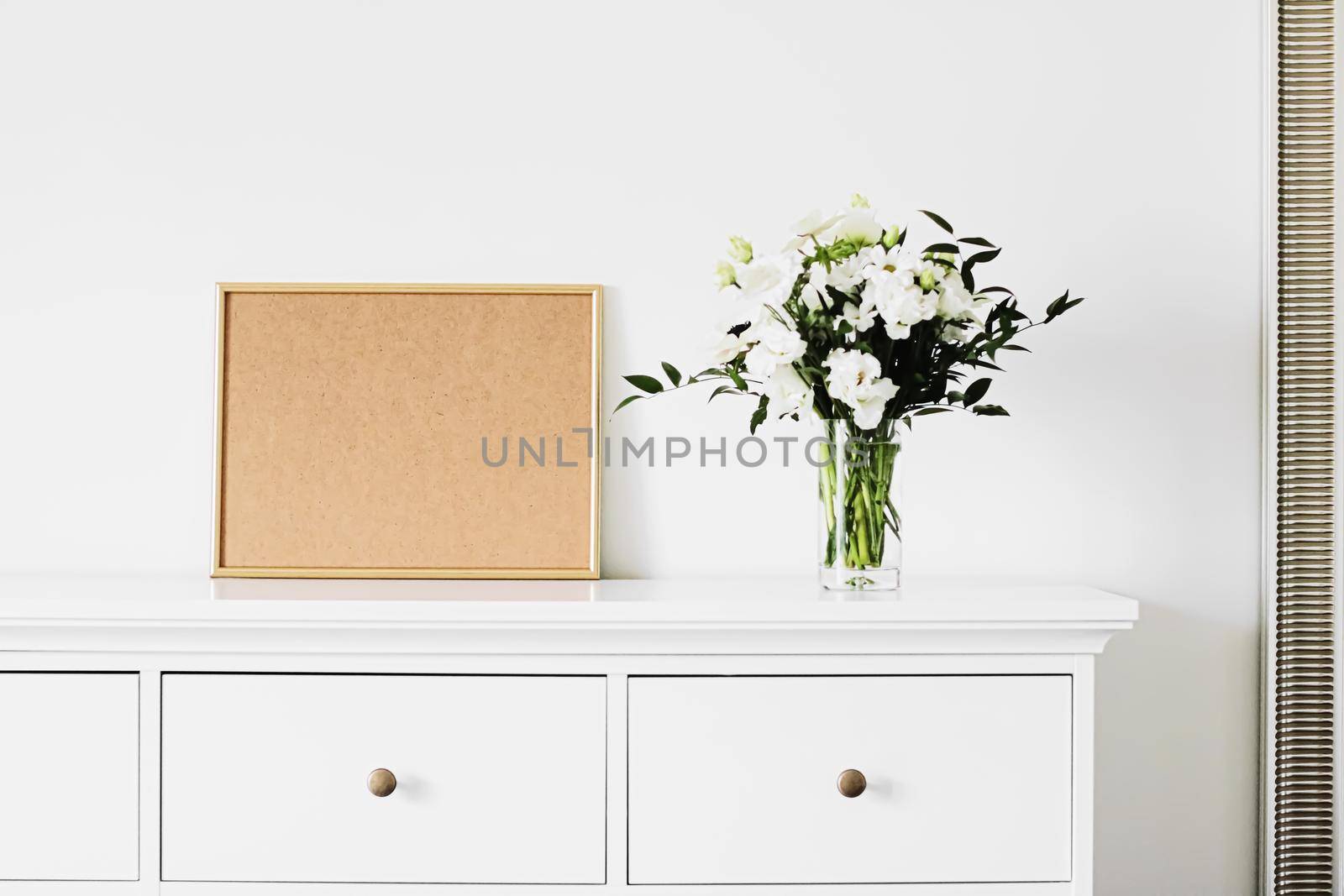 Golden horizontal frame and bouquet of fresh flowers on white furniture, luxury home decor and design for mockup creation by Anneleven