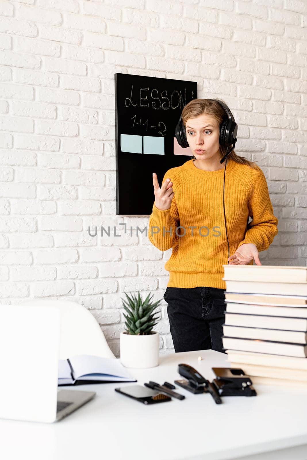 Distance learning. E-learning. Young smiling woman in yellow sweater and black headphones teaching online using video chat on laptop